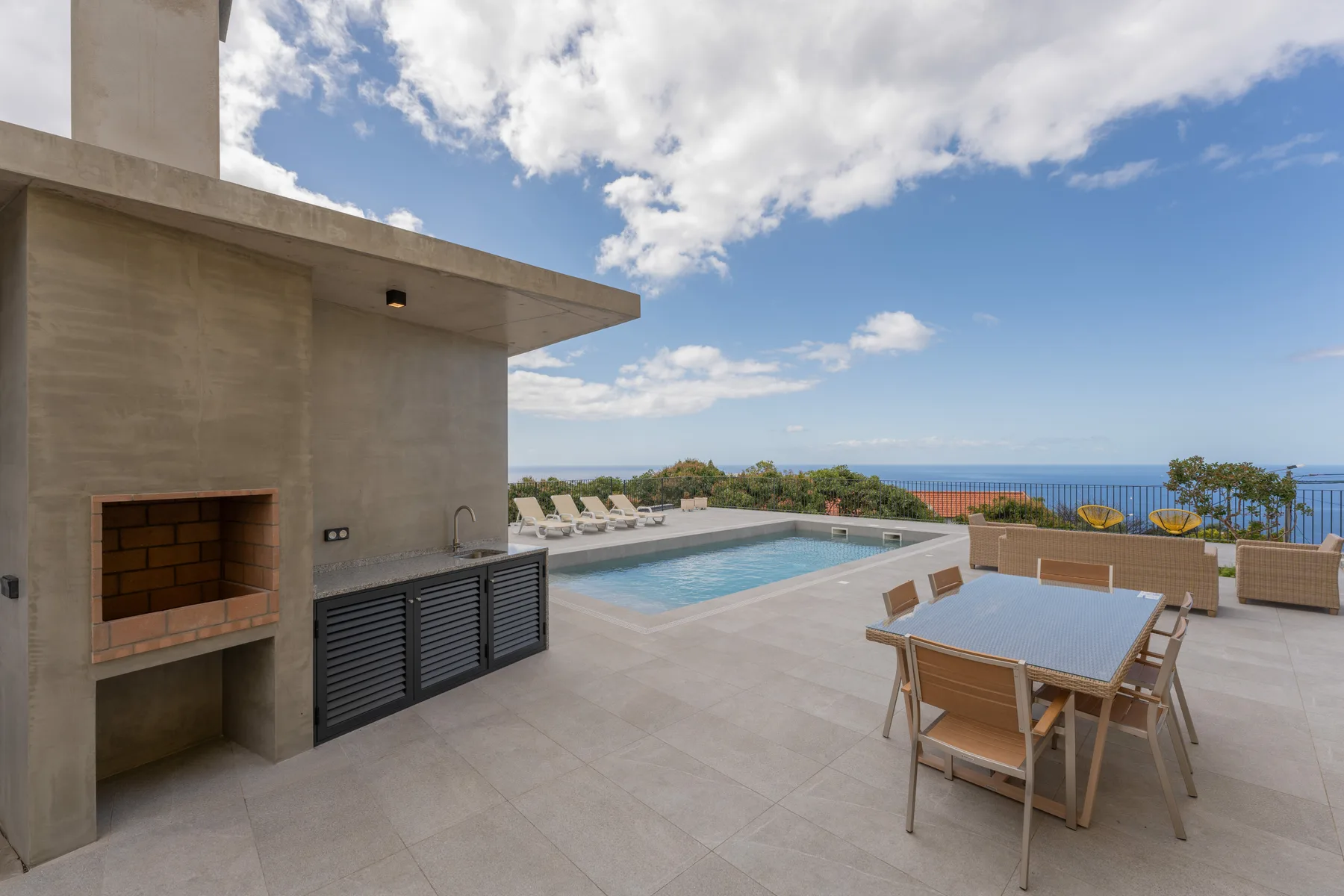 Una terraza soleada con piscina, mesa de comedor al aire libre y vistas al mar.