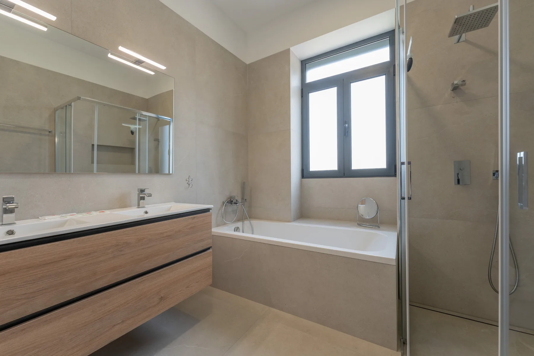 Un baño moderno con bañera, ducha de cristal y mueble de lavabo con frente de madera.