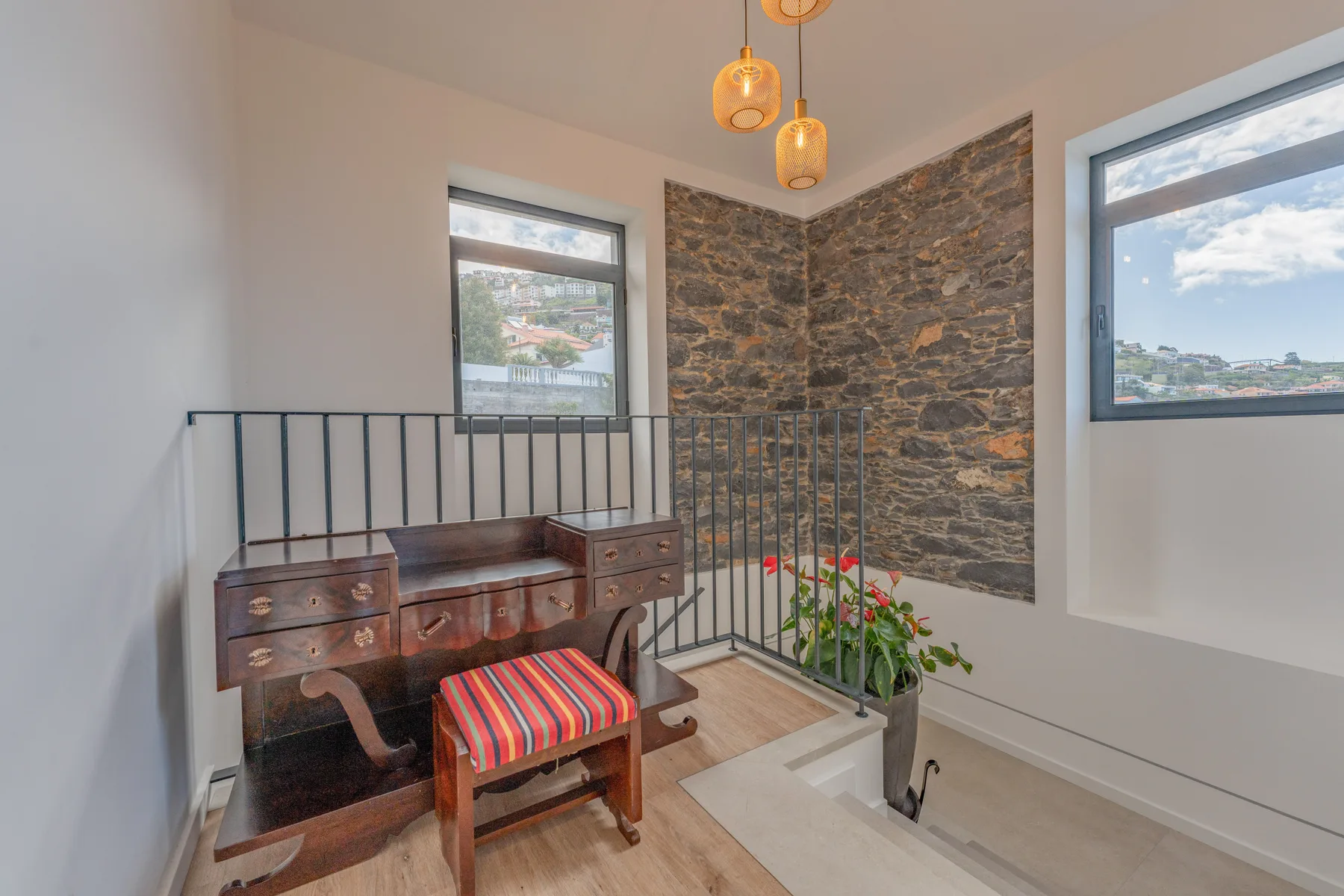 A stair landing with a wooden desk, striped seat, and stone accent wall.