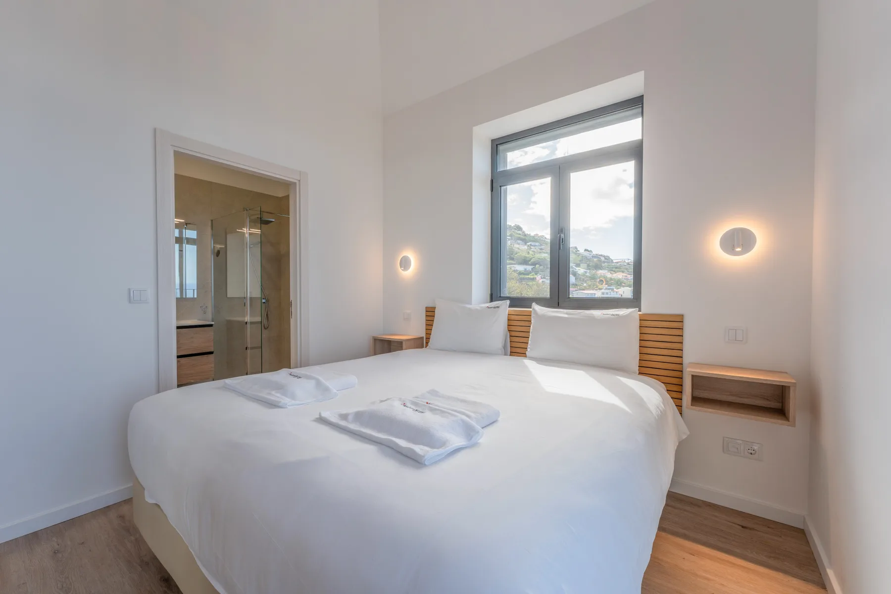 A bright bedroom with a neatly made bed beneath a large window.