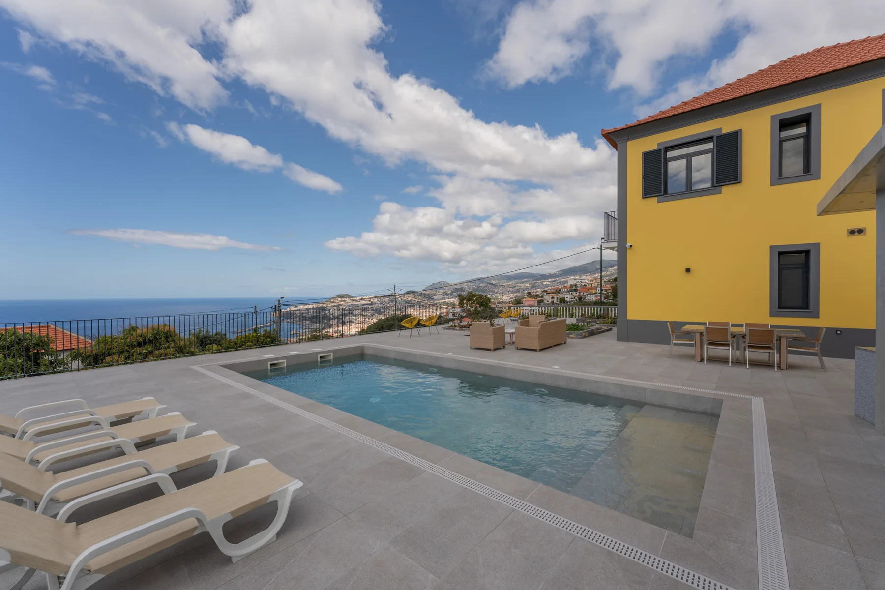 Una piscina y asientos de descanso miran al mar junto a un edificio amarillo.