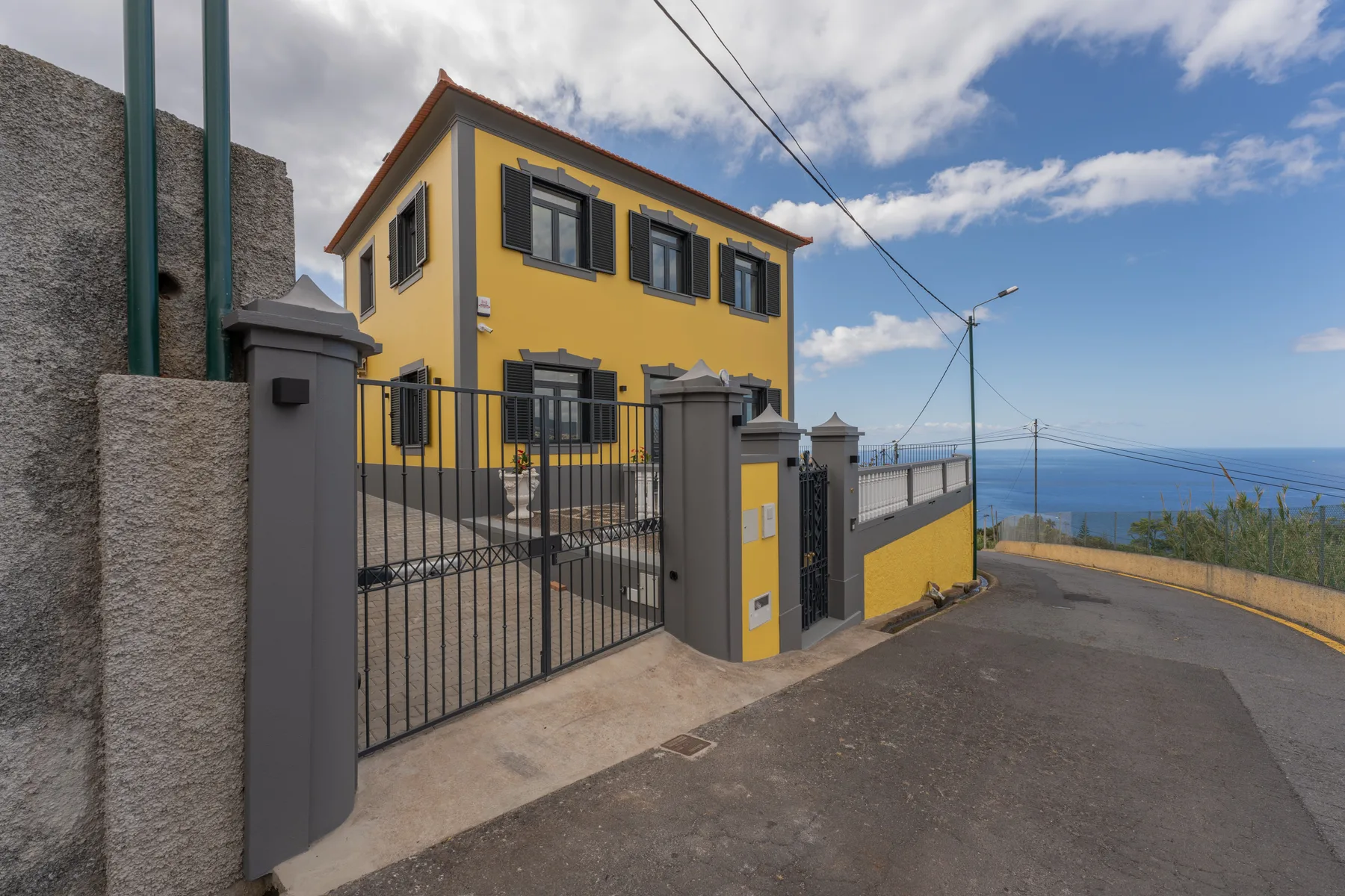Una casa amarilla de dos plantas se encuentra tras una entrada con verja junto a una carretera costera.