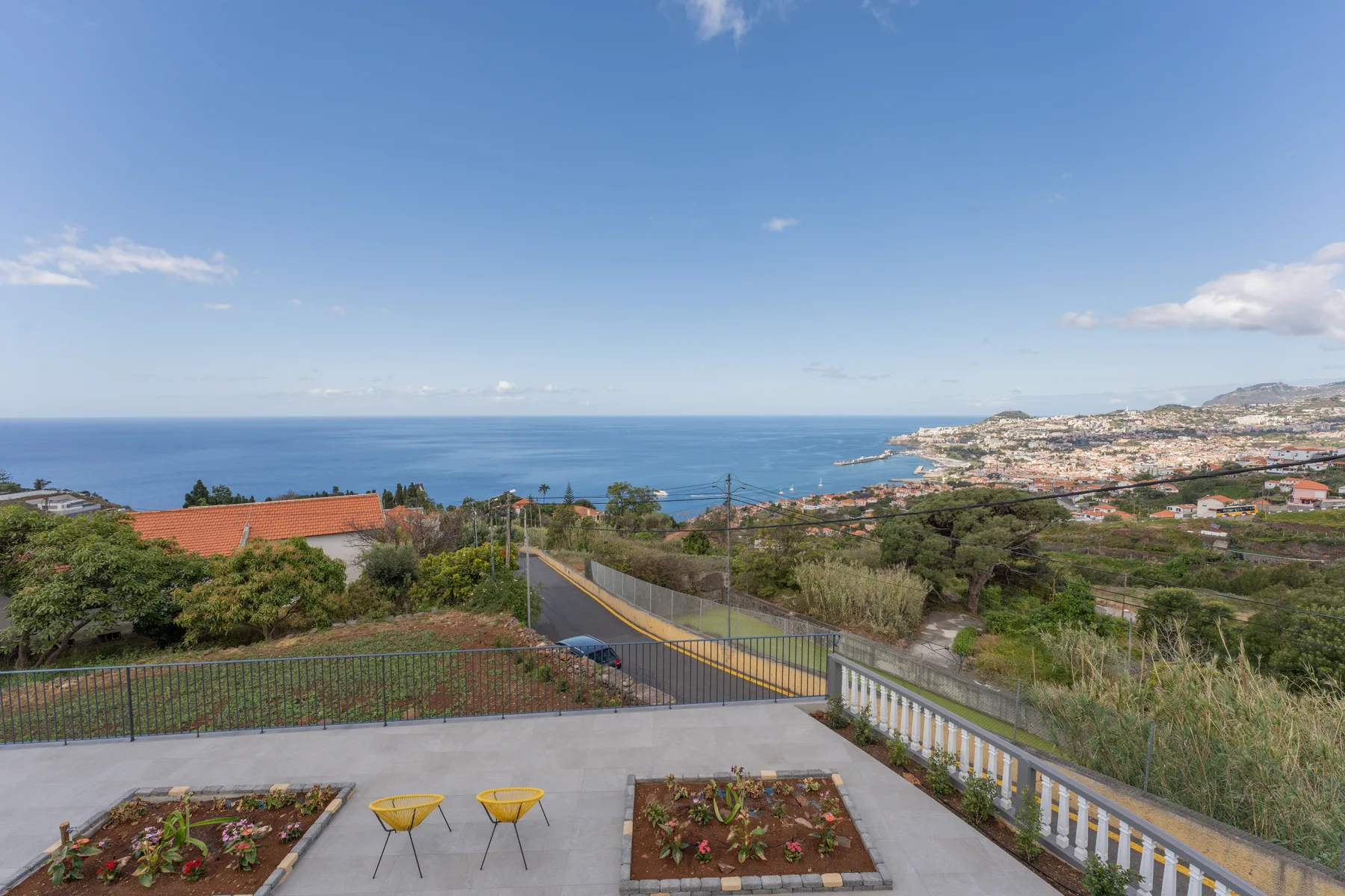 Una terraza pavimentada da a parterres, una carretera y el mar.