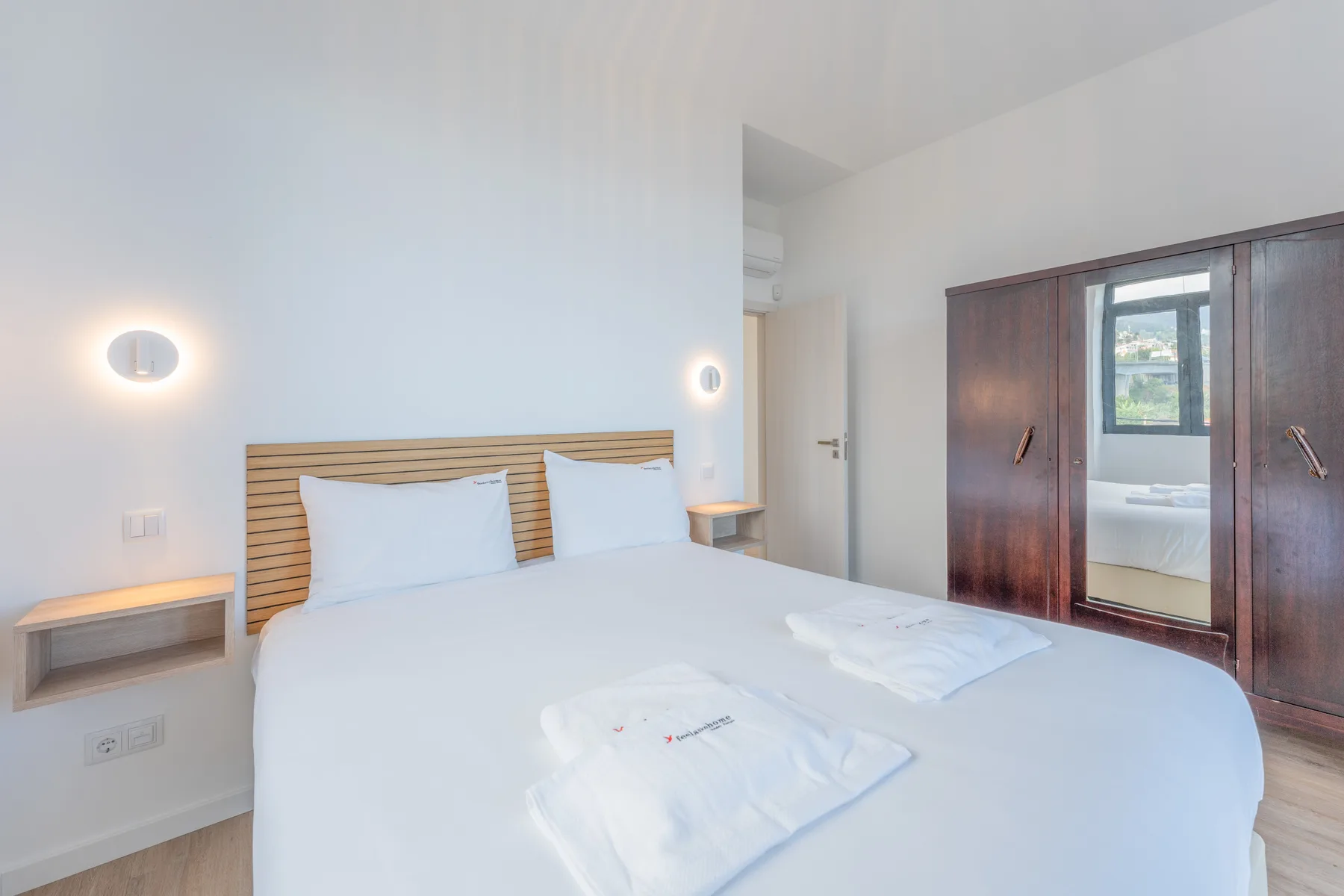 Un dormitorio luminoso con una cama doble, estantes junto a la cama y un armario con espejo.