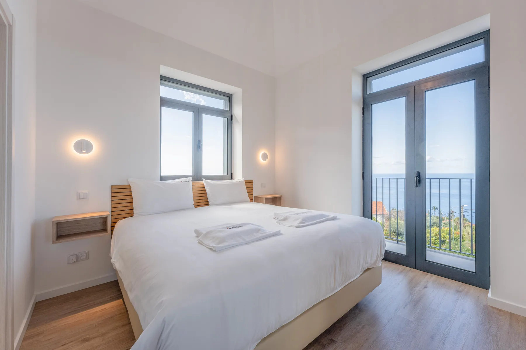 Un dormitorio luminoso con una cama arreglada y grandes ventanales con acceso a un balcón.