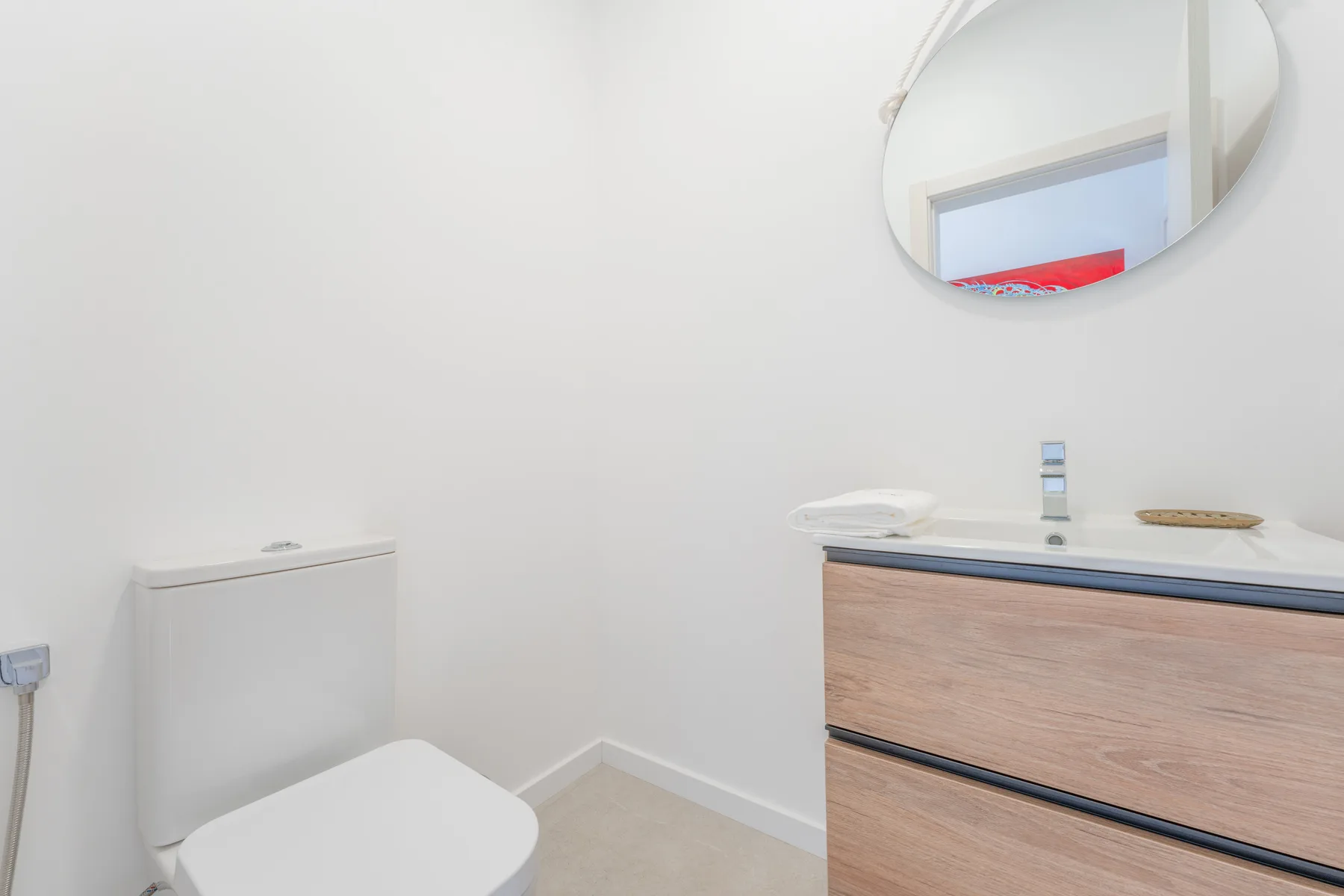 A bright bathroom with a toilet and a wood-front vanity.