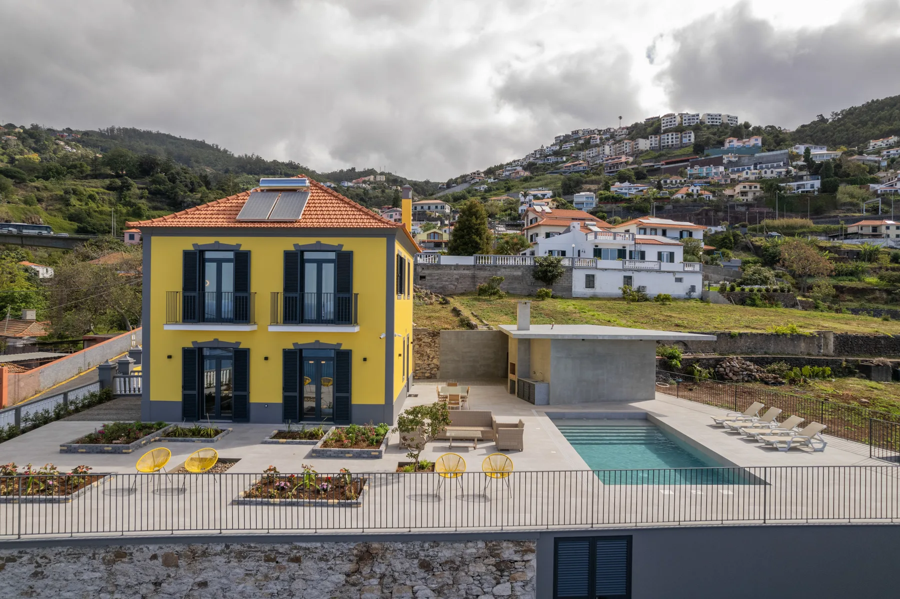 Una casa amarilla da a una piscina y a viviendas en la ladera.