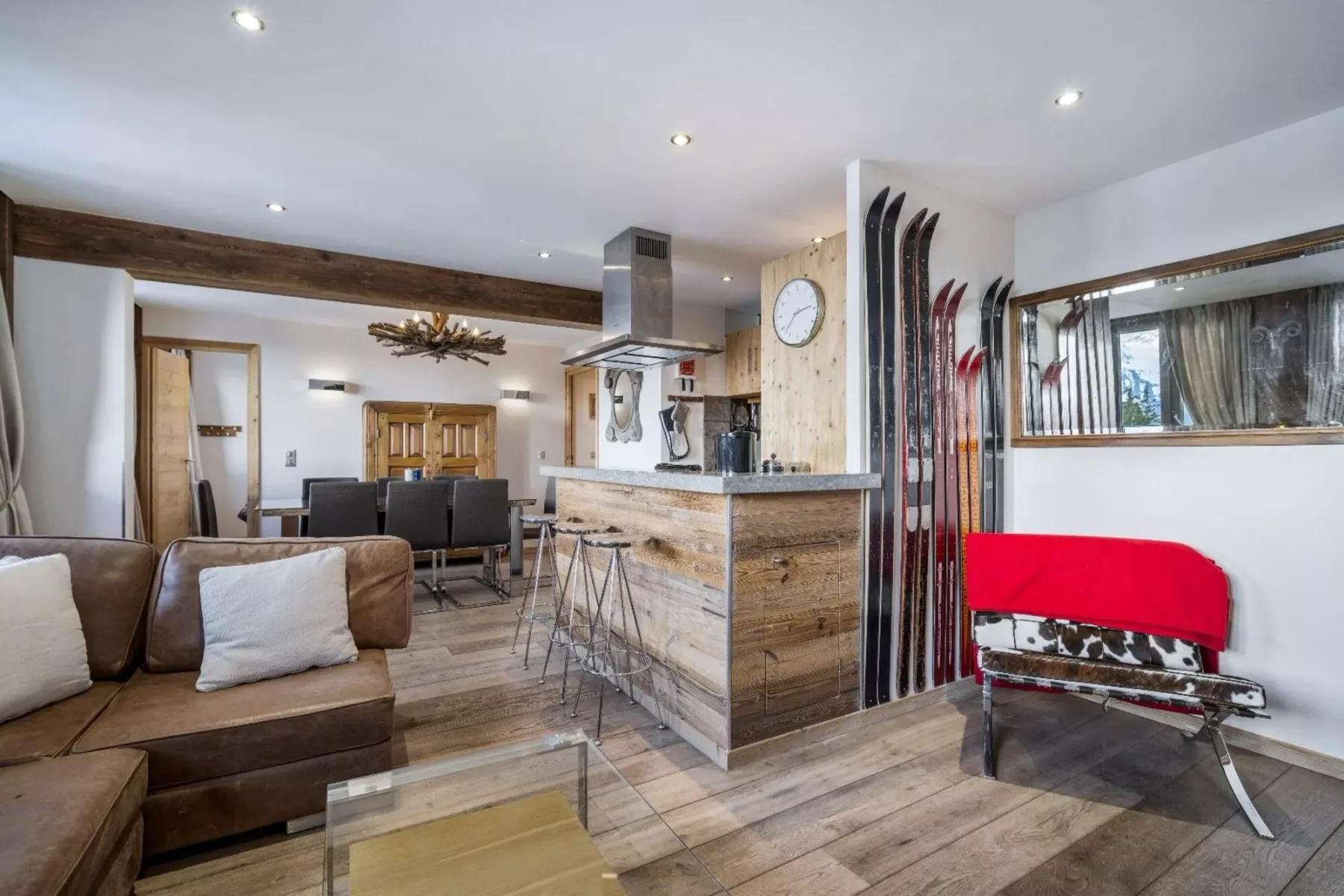 An open-plan living and dining area with a kitchen counter and skis displayed by the wall.