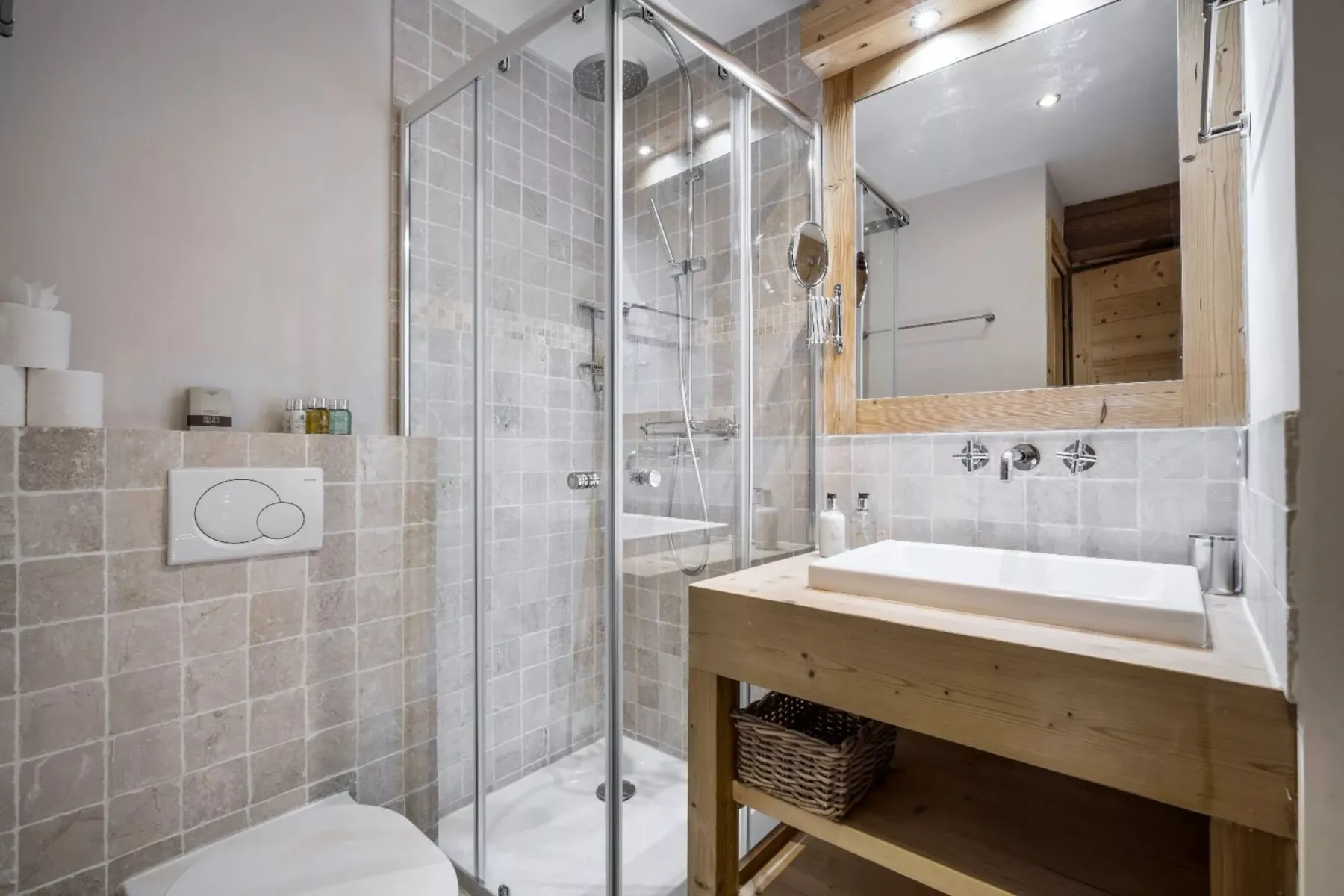 A tiled bathroom with a glass shower and a wooden vanity beneath a mirror.