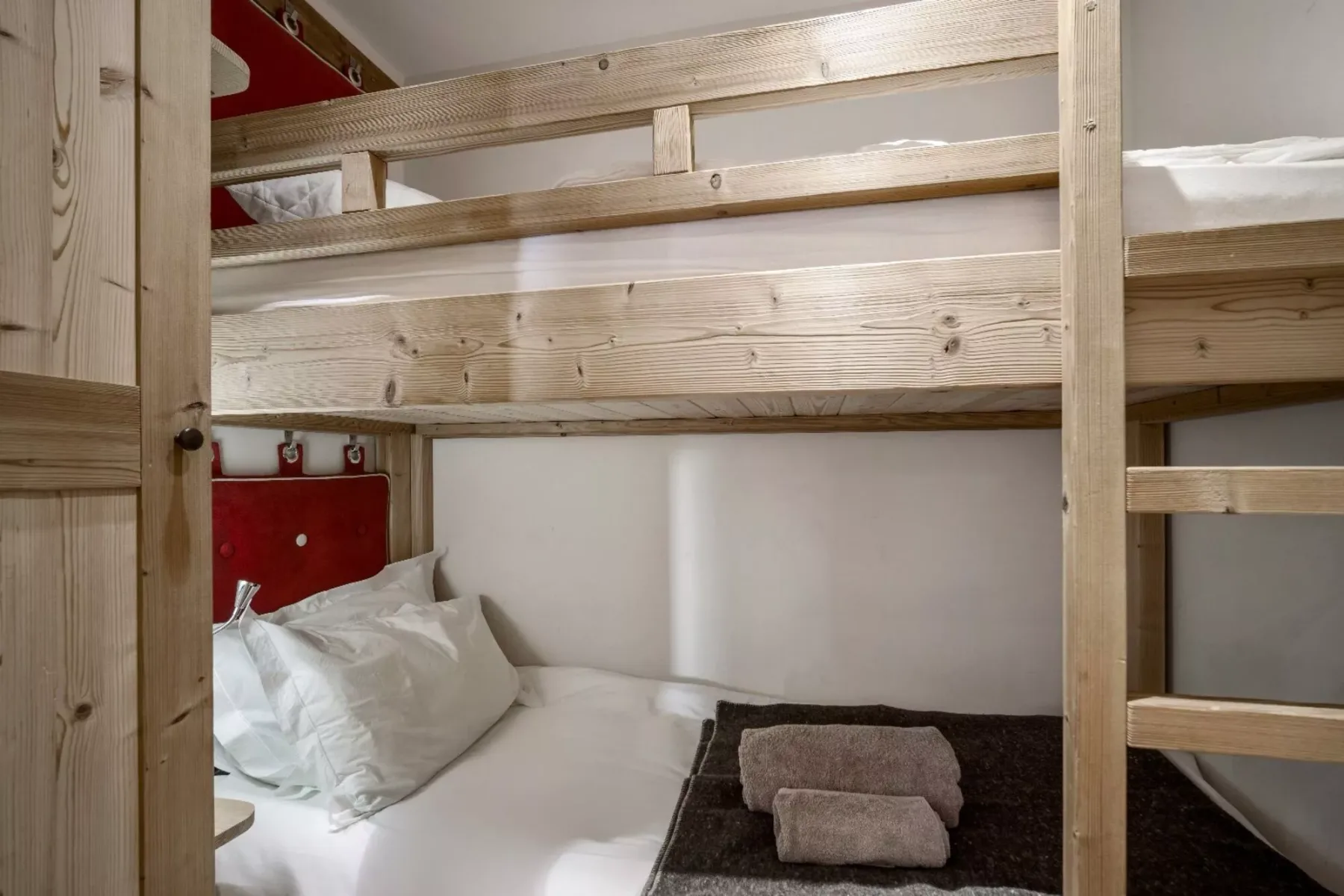 A bunk bed with white bedding and folded towels in a compact bedroom.