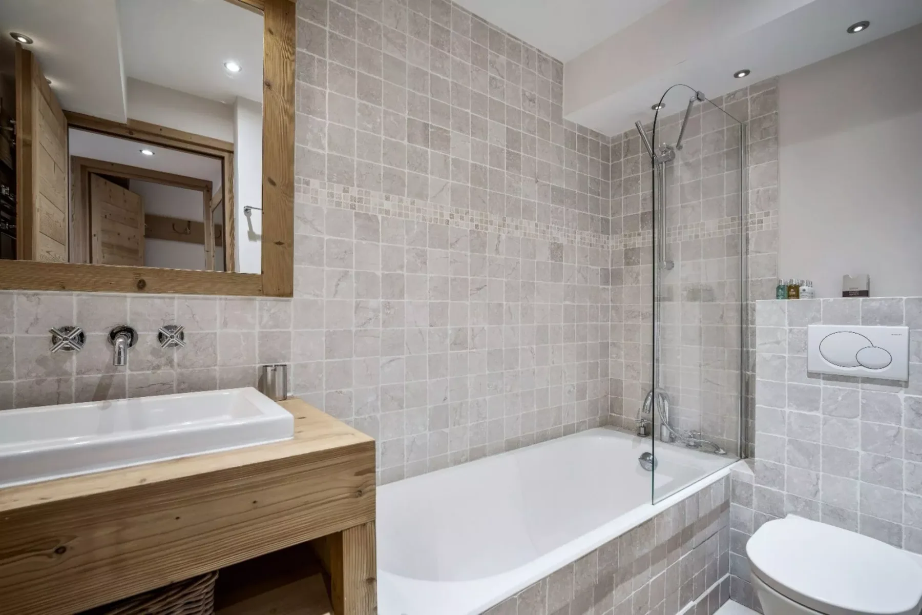 A tiled bathroom with a bathtub, sink, and wall-mounted mirror.