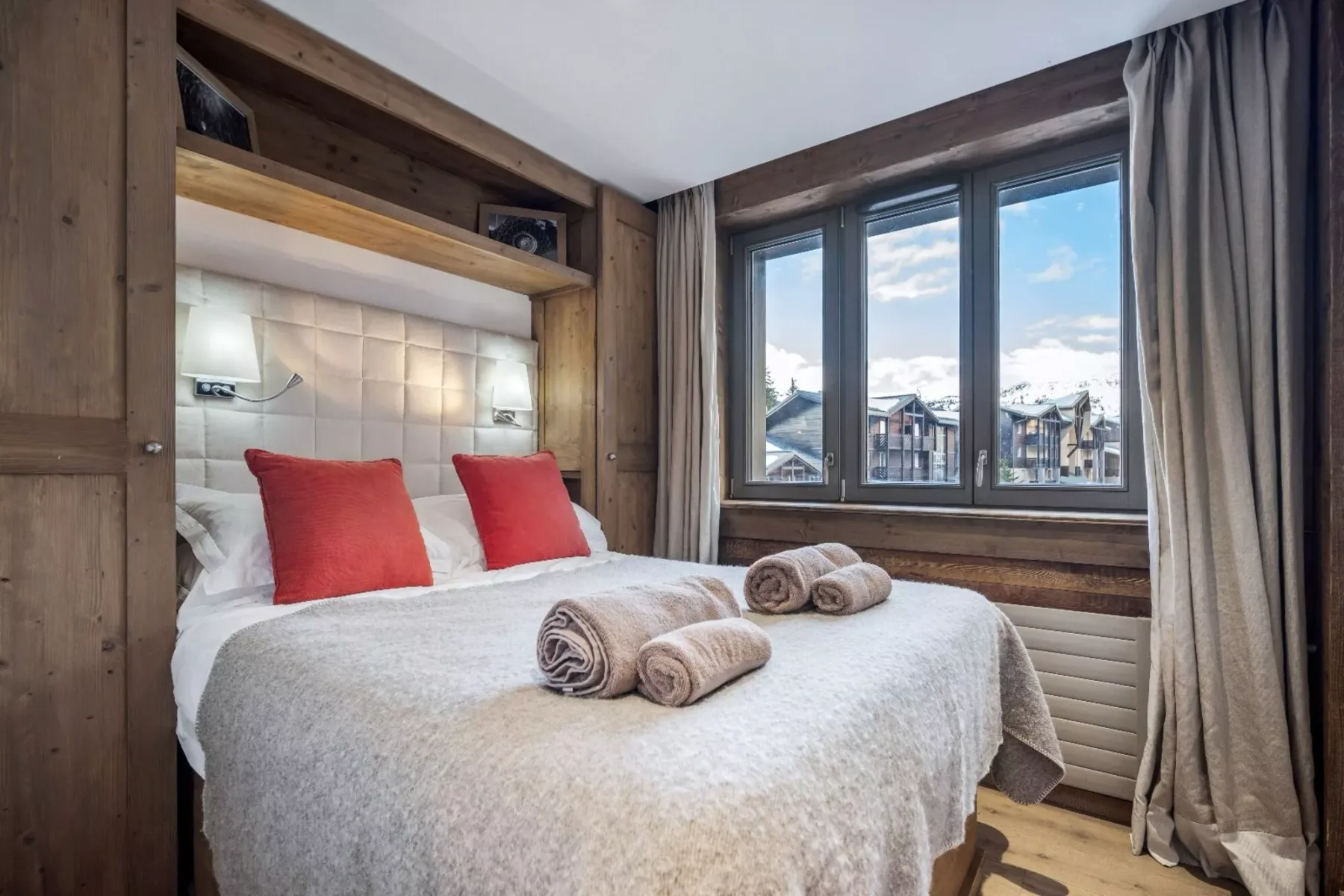 A bedroom with a double bed and a large window overlooking nearby buildings.