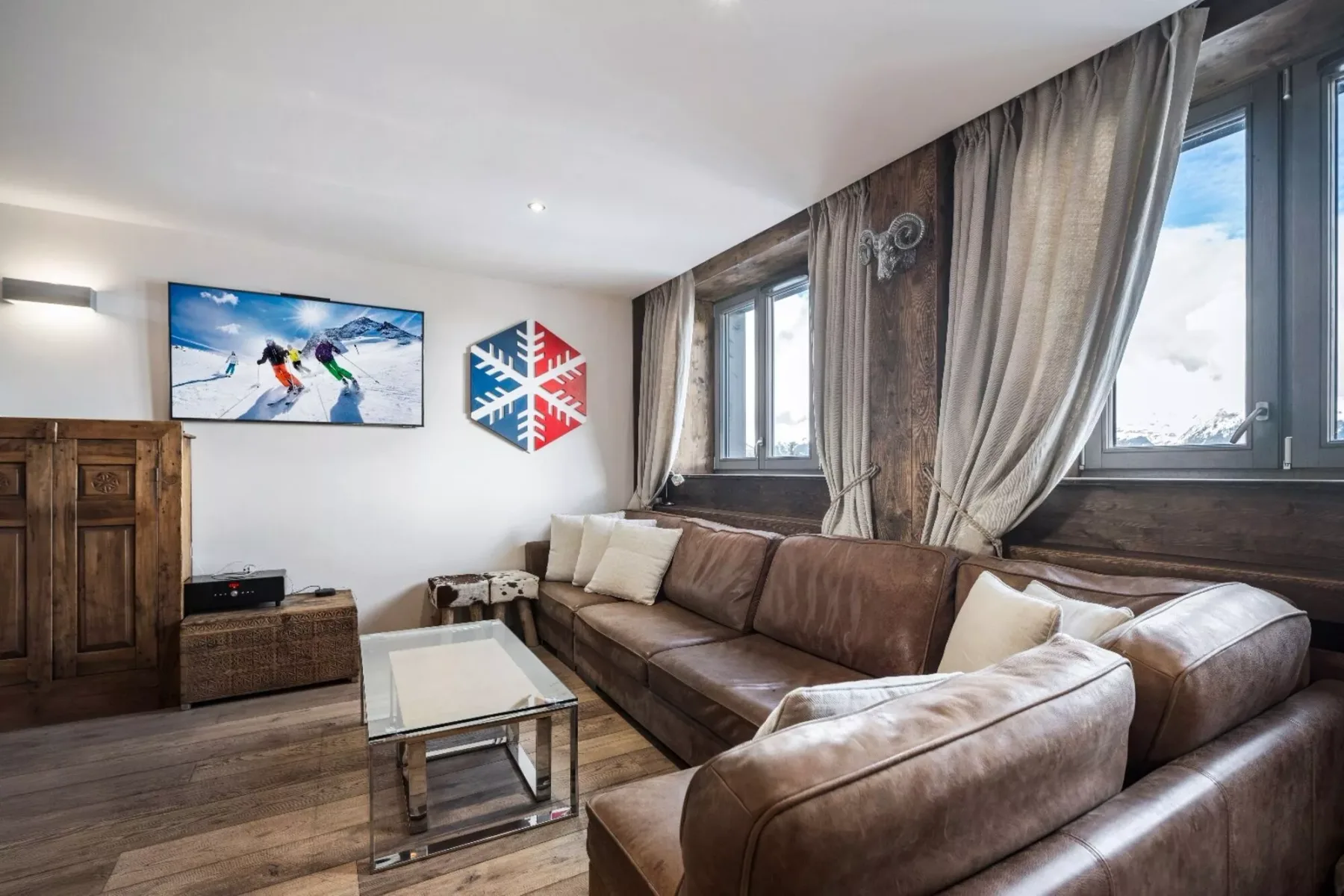 A living room with brown seating, a glass coffee table, and snowy mountain views.