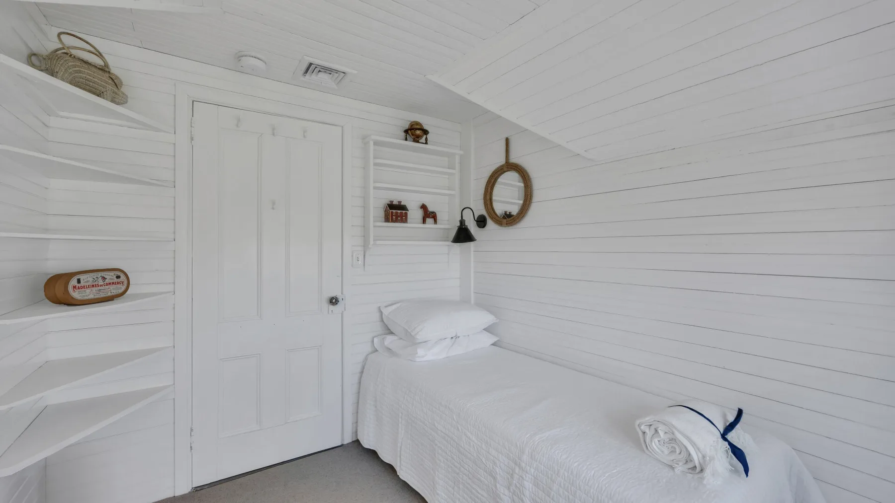A bright bedroom with a white bed and paneled walls.