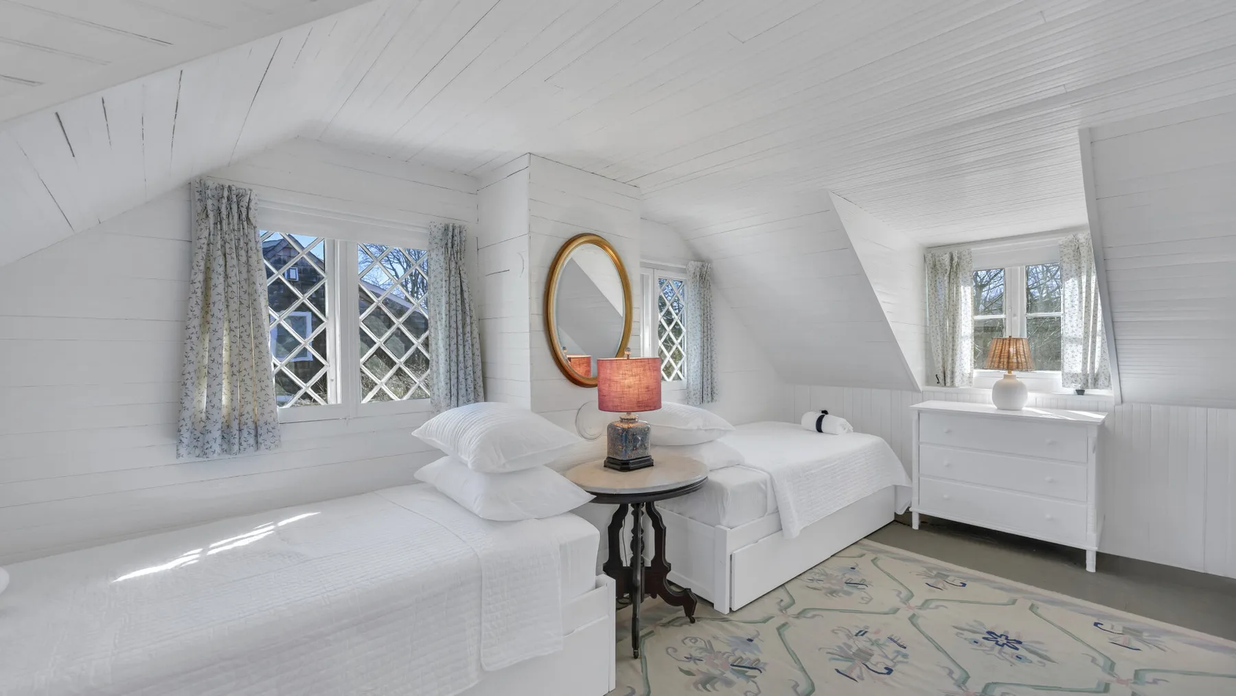 A bright bedroom with two beds, a bedside table, and a dresser.