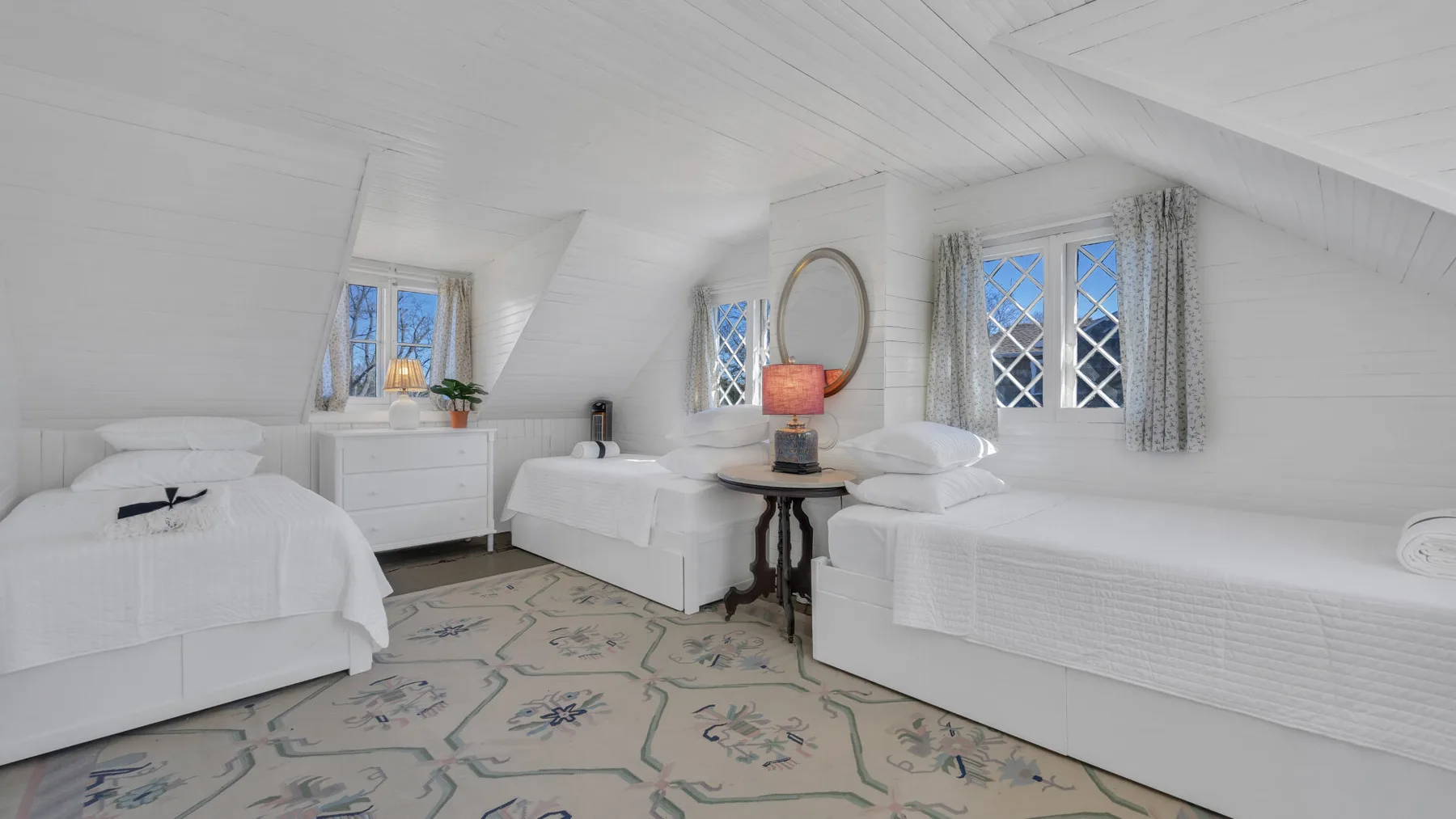 A bright attic bedroom with several beds and windows along the sloped walls.