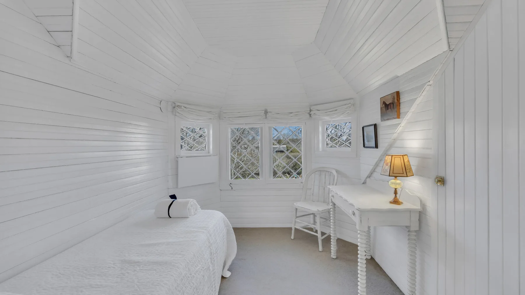 A bright bedroom with a bed and a desk beside the windows.