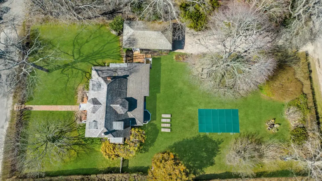 An aerial view of a house and green lawn with a rectangular blue court.
