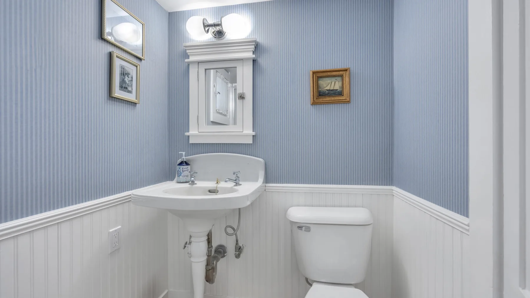 A bathroom with a sink, toilet, and framed pictures on pale blue walls.