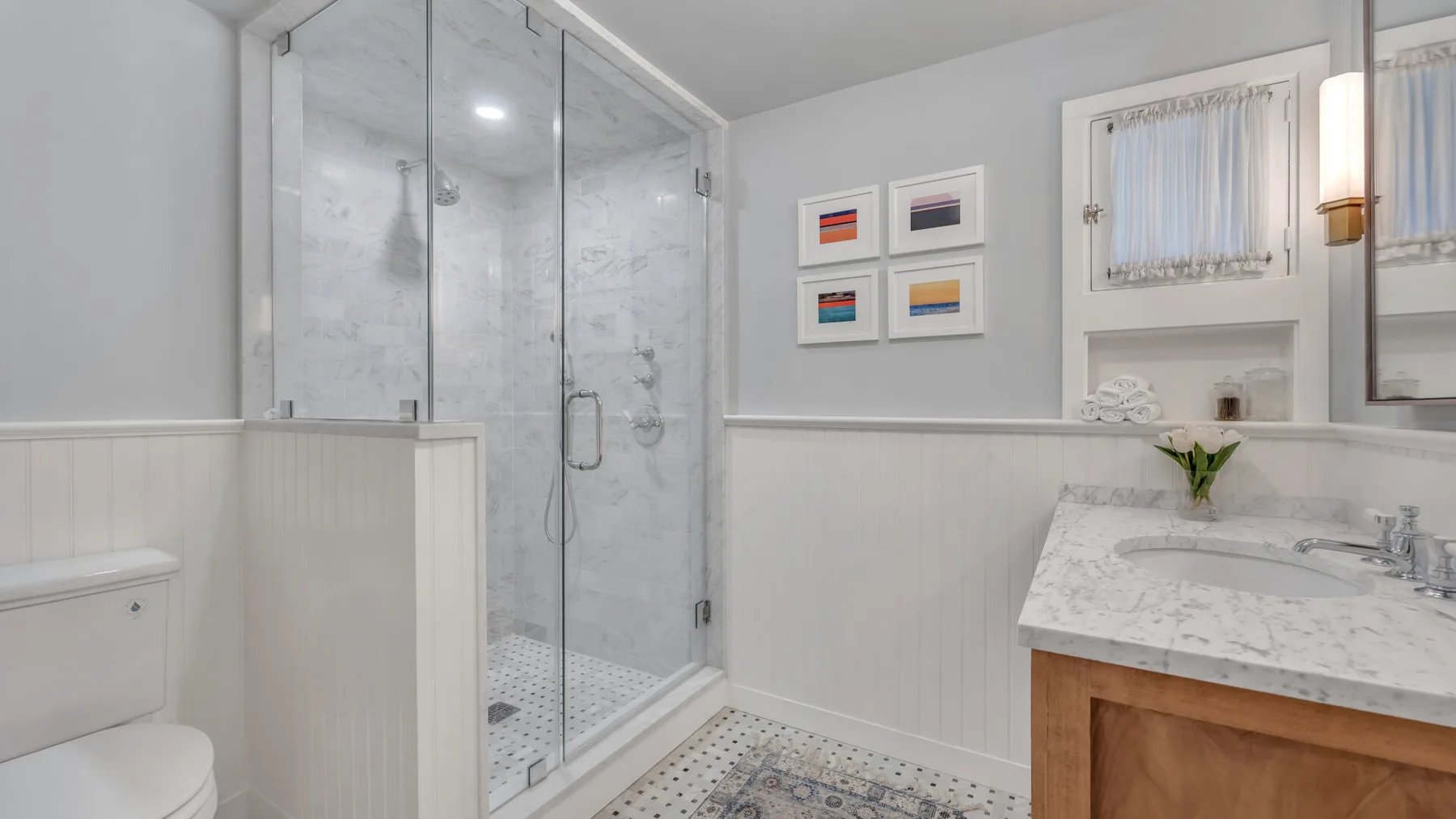 A bright bathroom with a glass shower and a marble vanity.