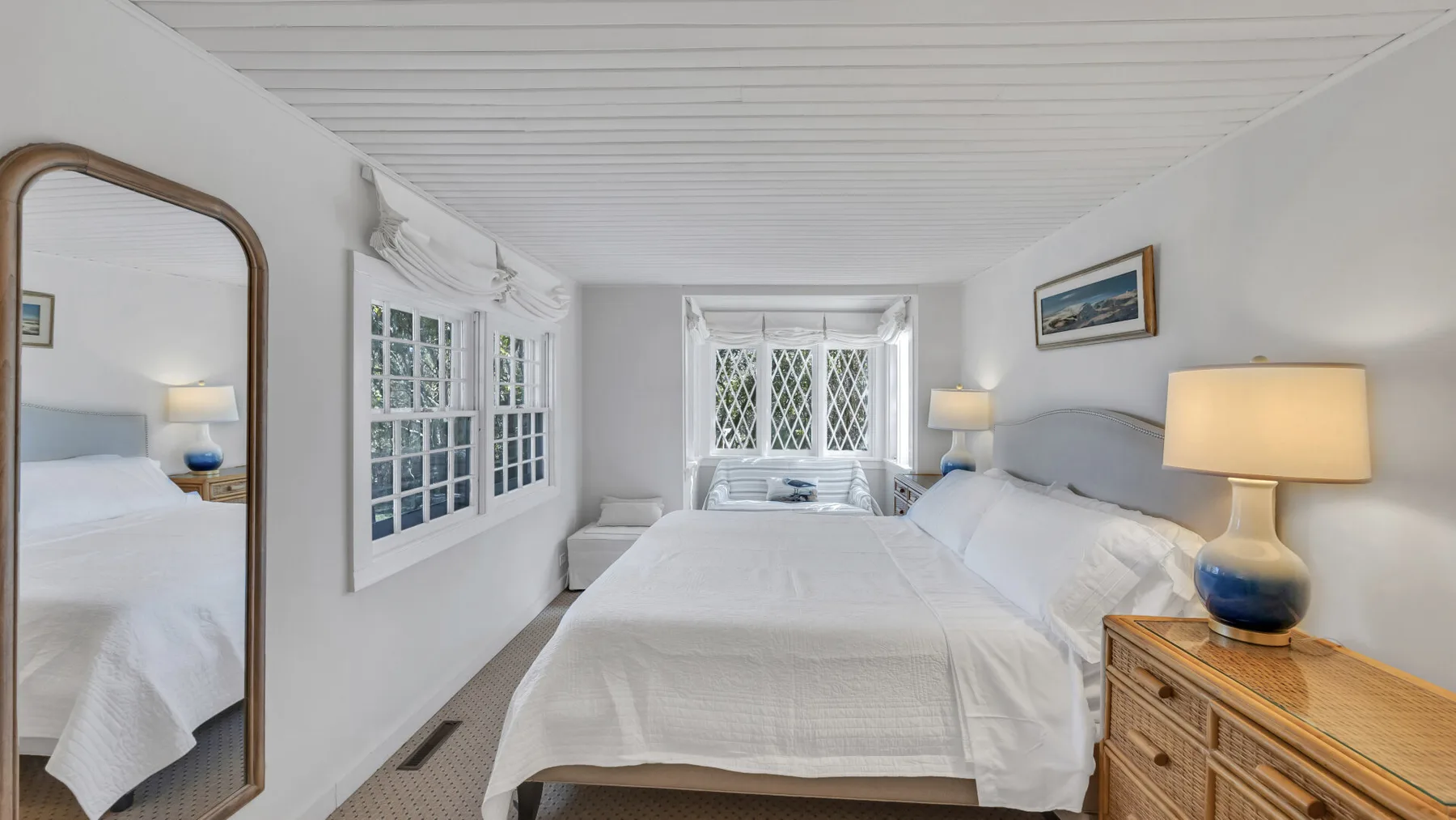 A bright bedroom with a neatly made bed and large windows.
