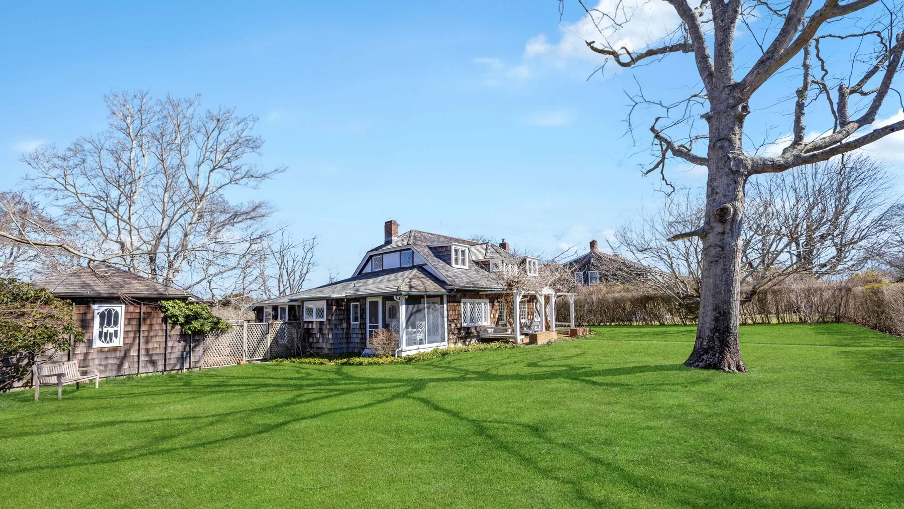 A large house stands beside a broad green lawn and leafless trees.