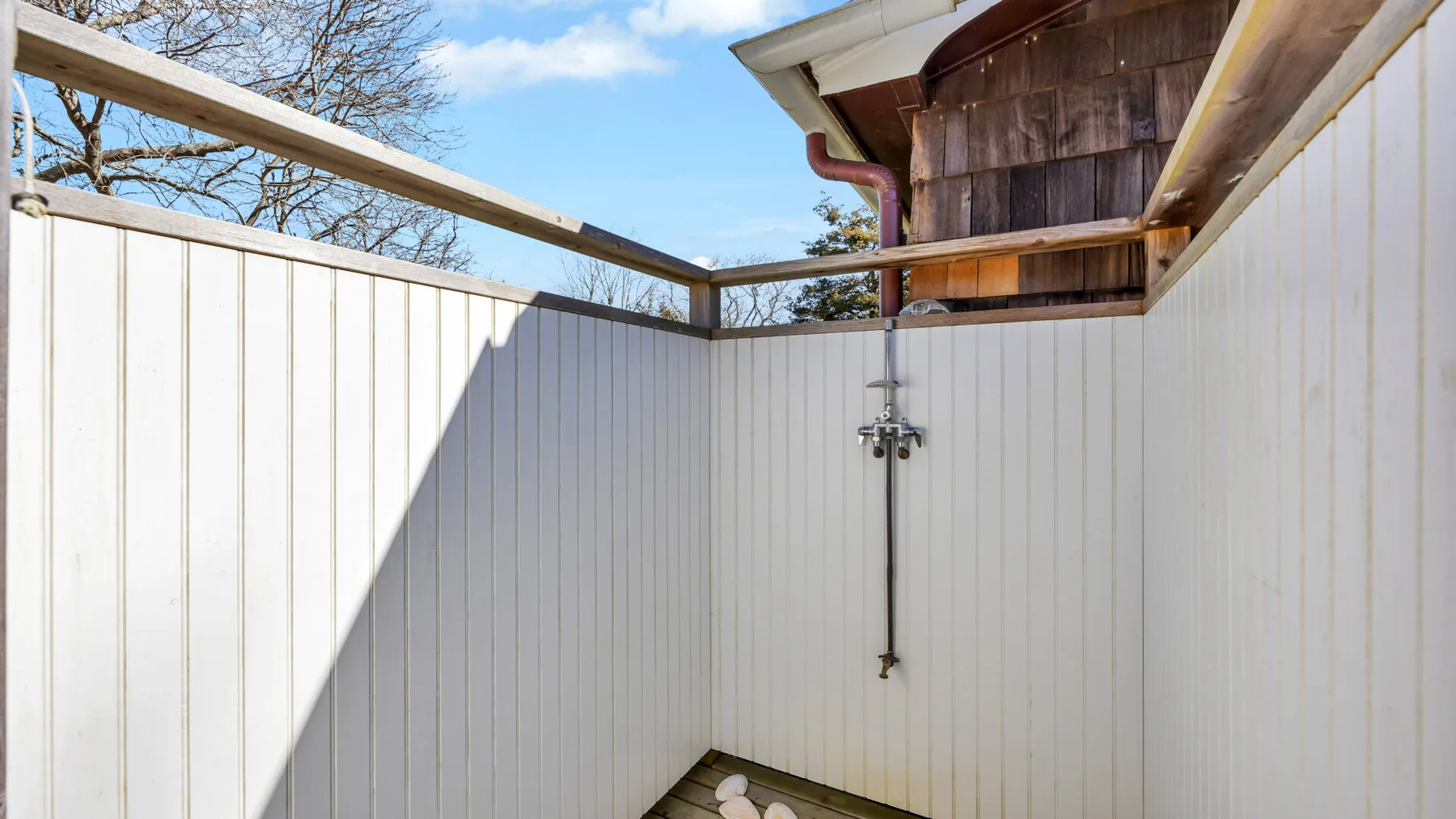 An outdoor shower area with white privacy walls and an overhead shower fixture.