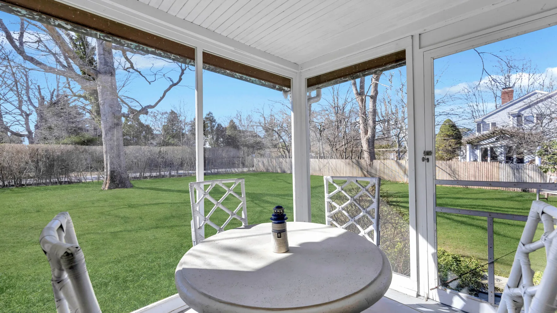 A covered patio dining area overlooks a green lawn and trees.