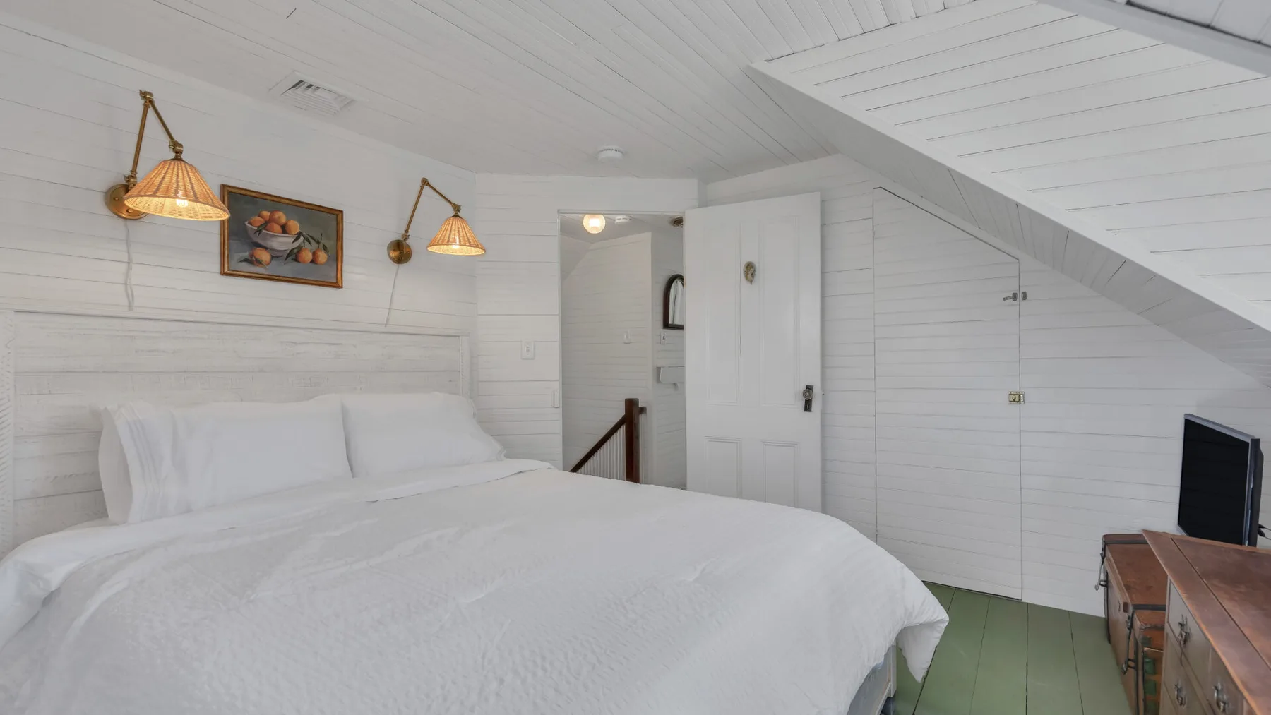 A bedroom with a bed beneath a sloped white ceiling.