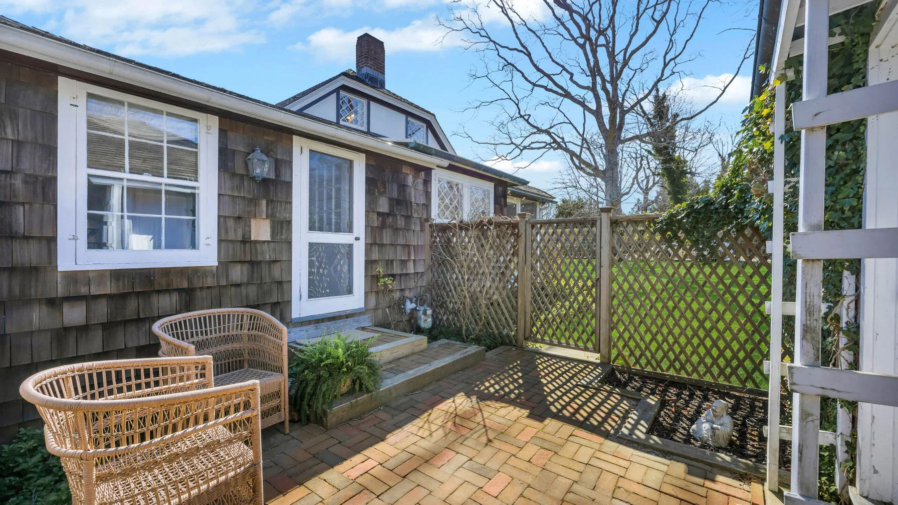 A paved outdoor patio beside a house, with wicker seating and a lattice fence.