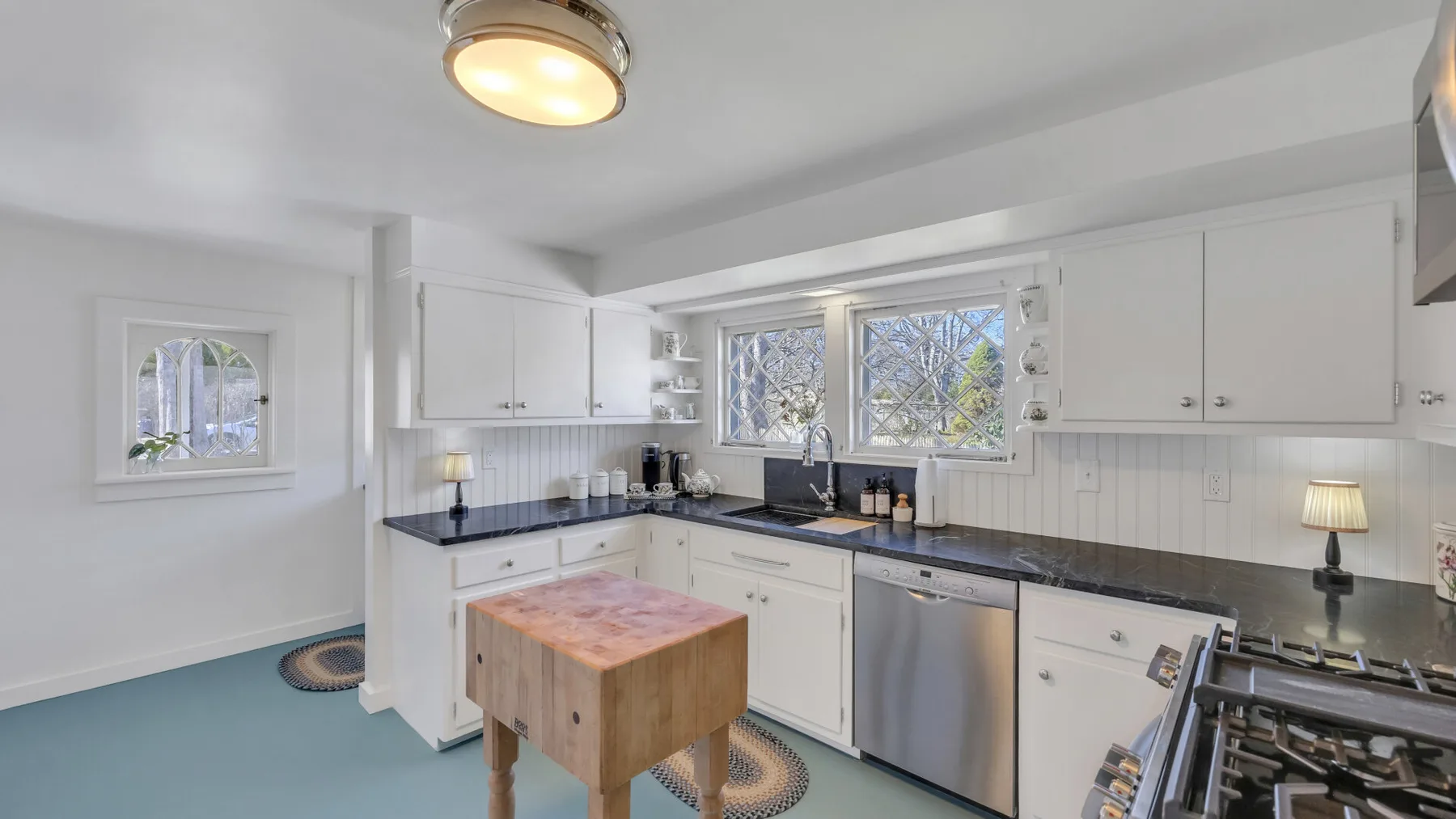 A bright kitchen with white cabinets, dark countertops, and a wooden island.