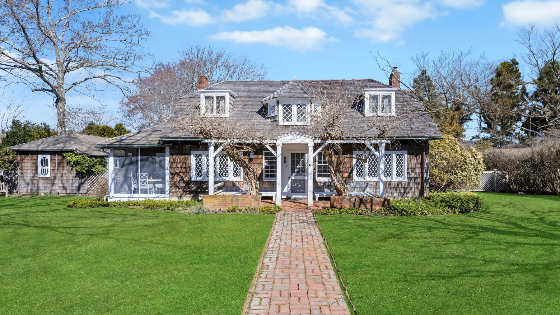A house stands beyond a brick path crossing a broad green lawn.