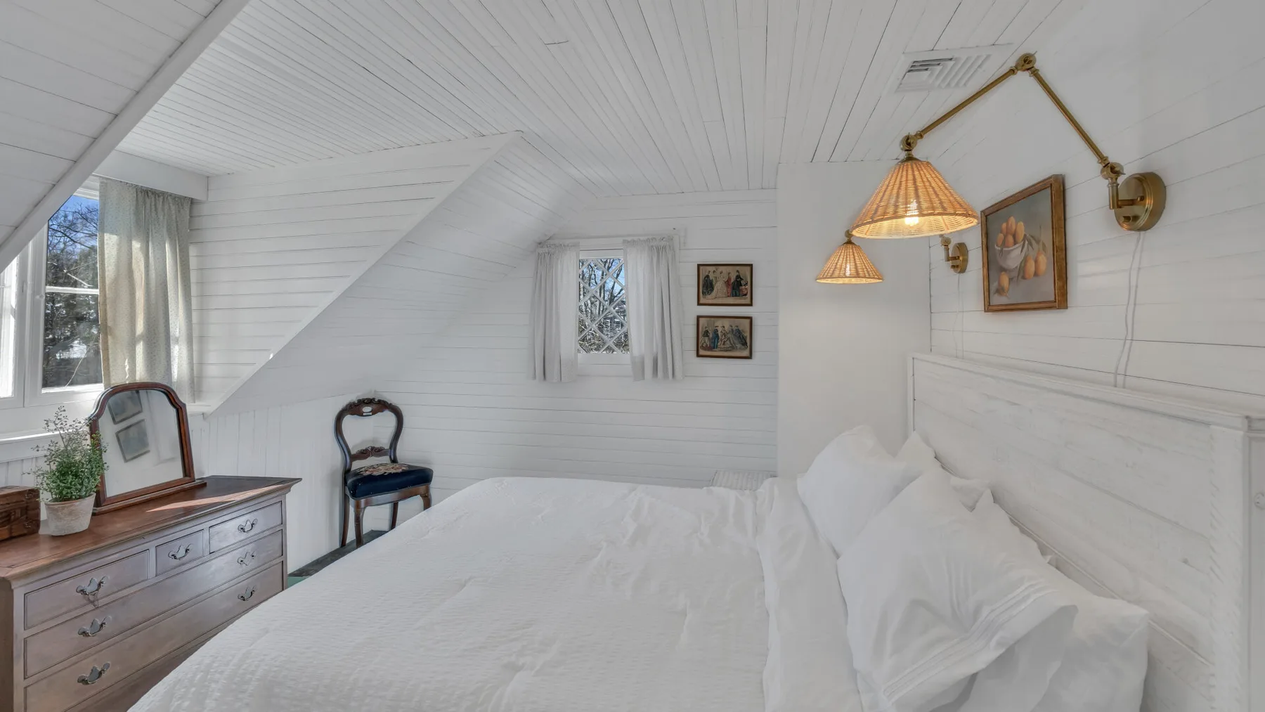 A bright bedroom with a white bed beneath a sloped ceiling.
