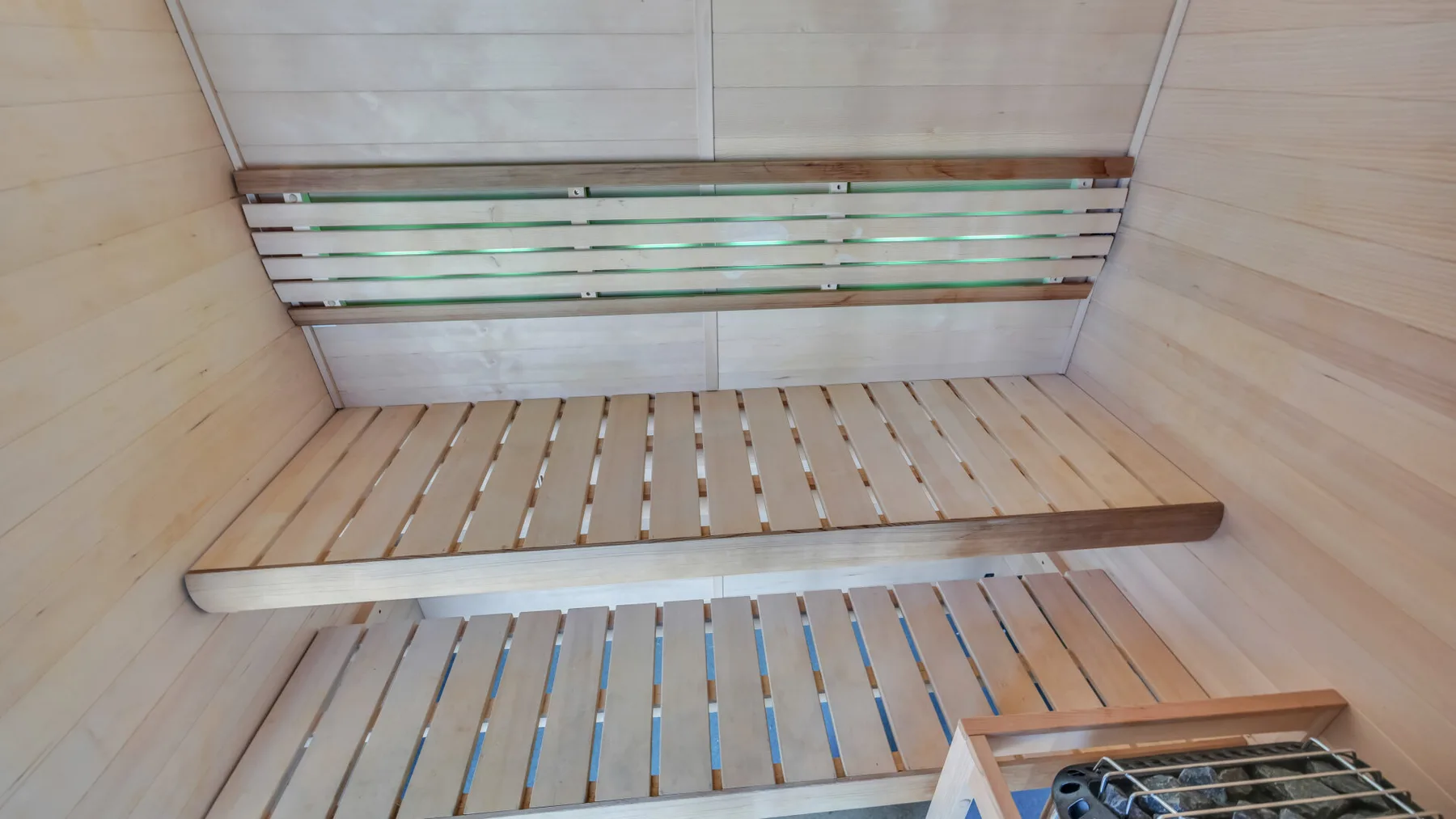 A wood-lined sauna room with slatted benches and a heater.