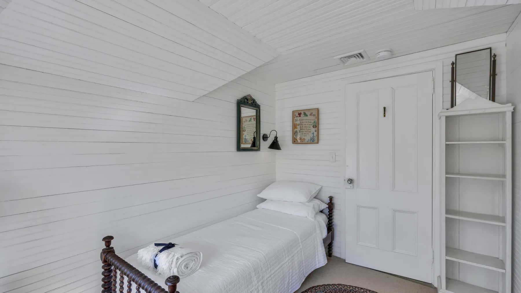 A bedroom with white bedding and a built-in shelving unit beside the door.