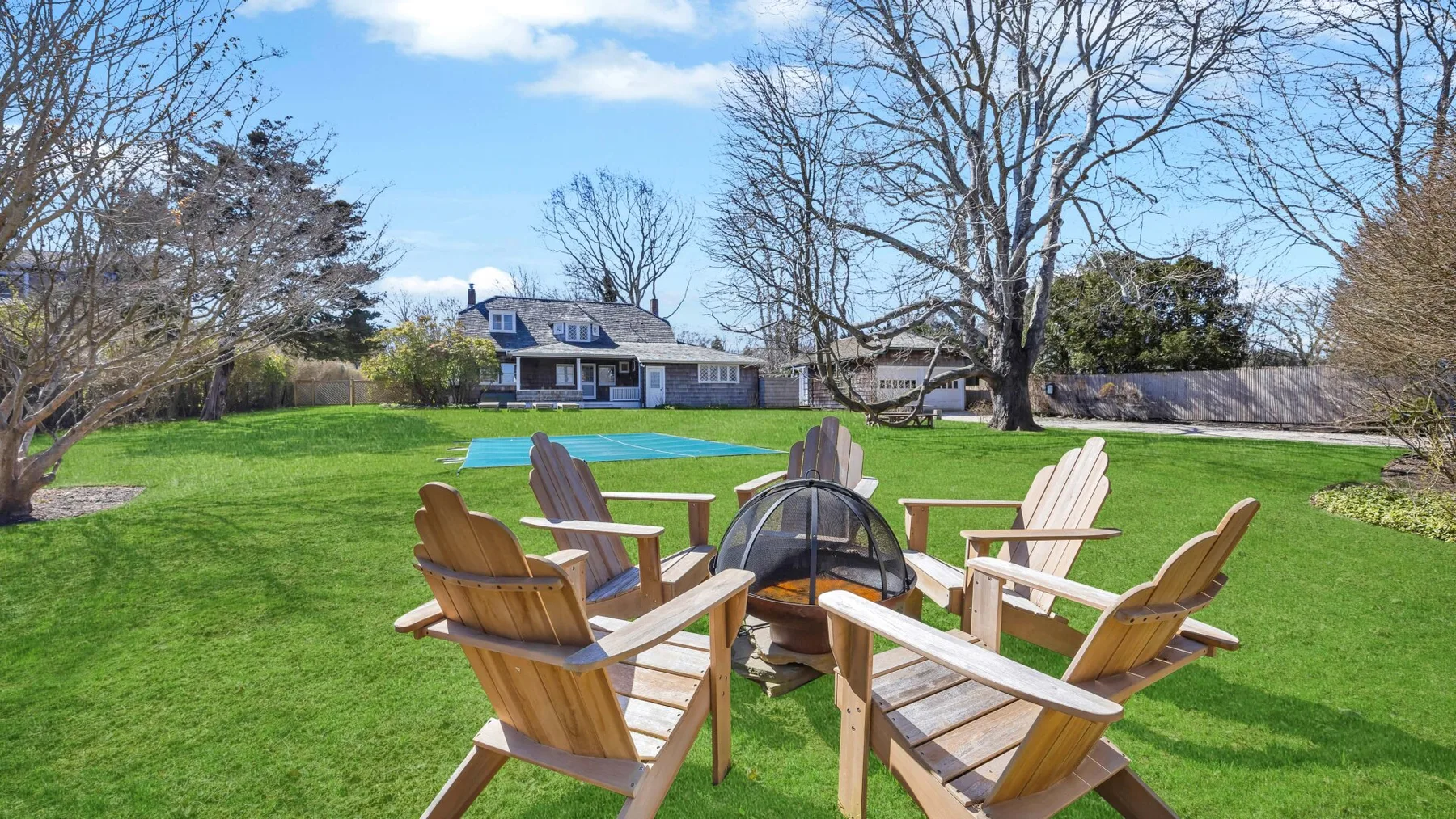 A grassy backyard with wooden seating arranged around a fire pit.