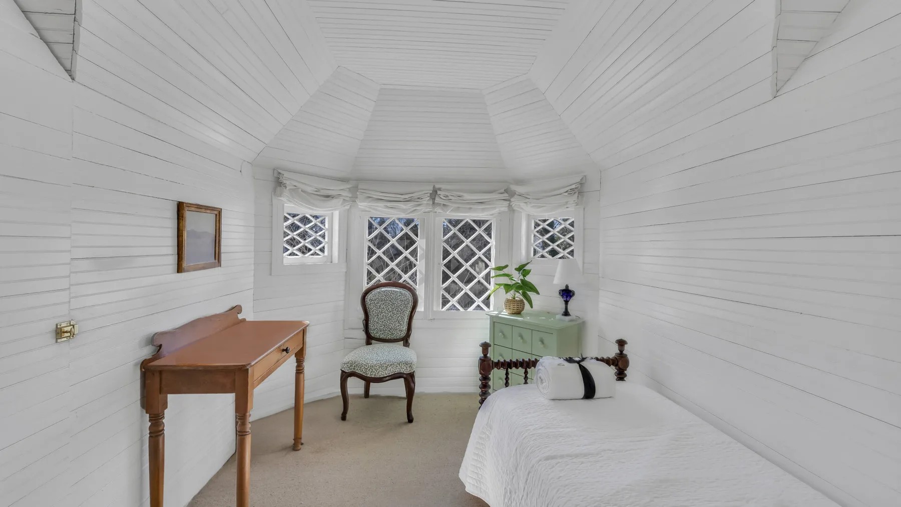 A bright white bedroom with a single bed, a chair, and windows.