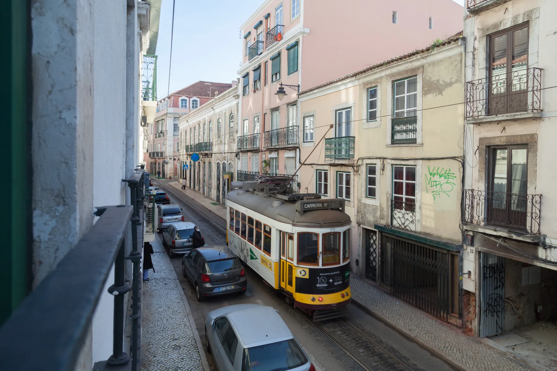 Un tranvía amarillo recorre una calle estrecha bordeada de edificios y coches aparcados.