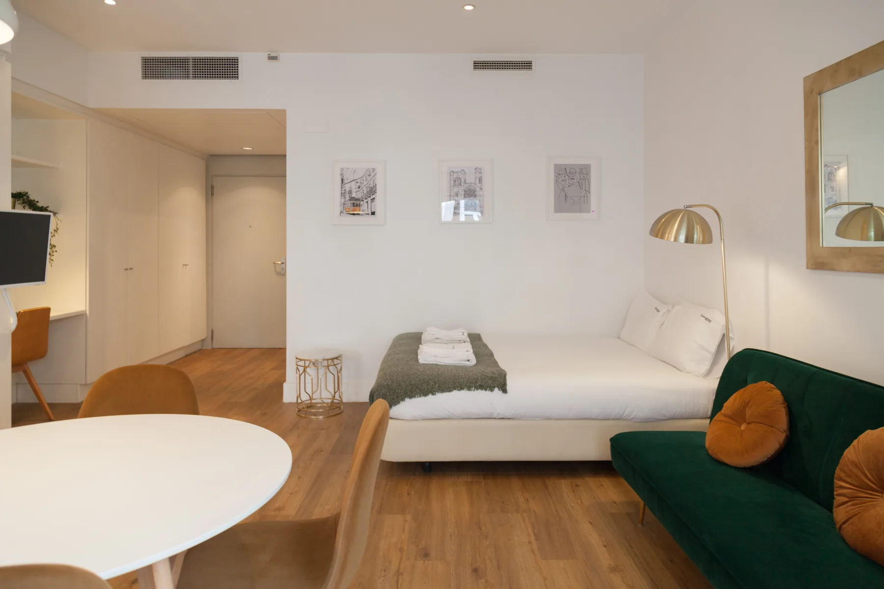 Un estudio con una cama, un sofá verde y una mesa redonda de comedor.