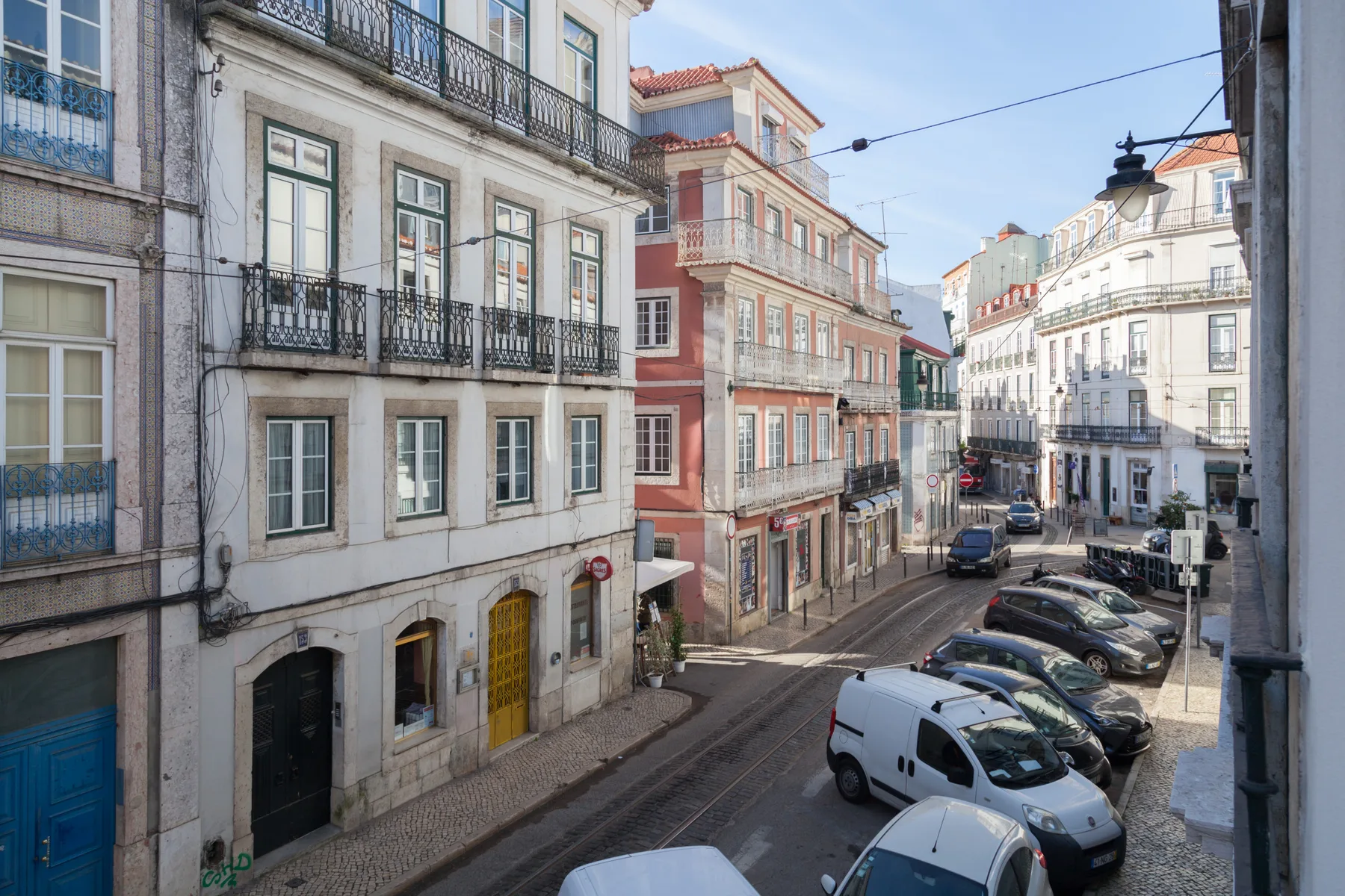 Una calle urbana bordeada de edificios de varias plantas y vehículos estacionados.