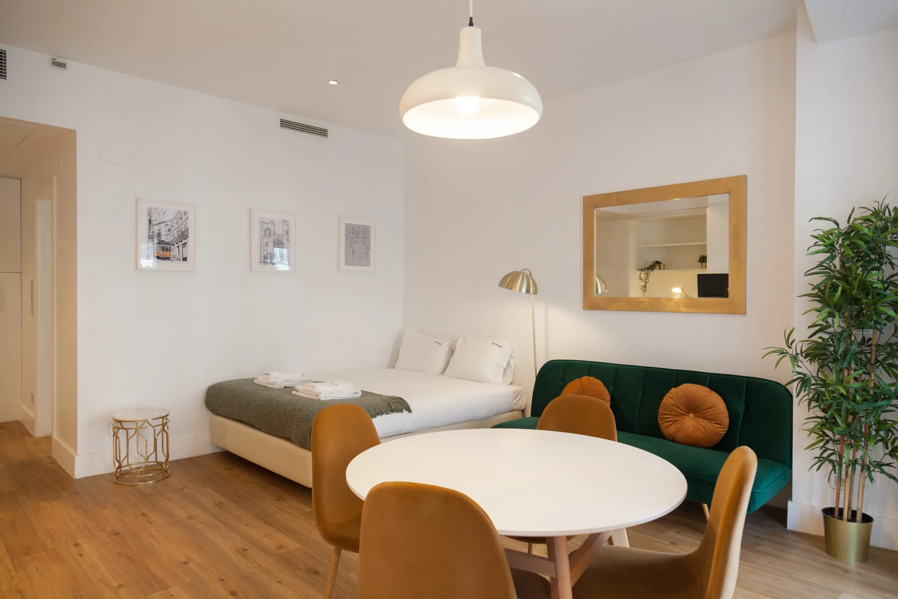 Un estudio combina una cama, asientos verdes y una mesa redonda.