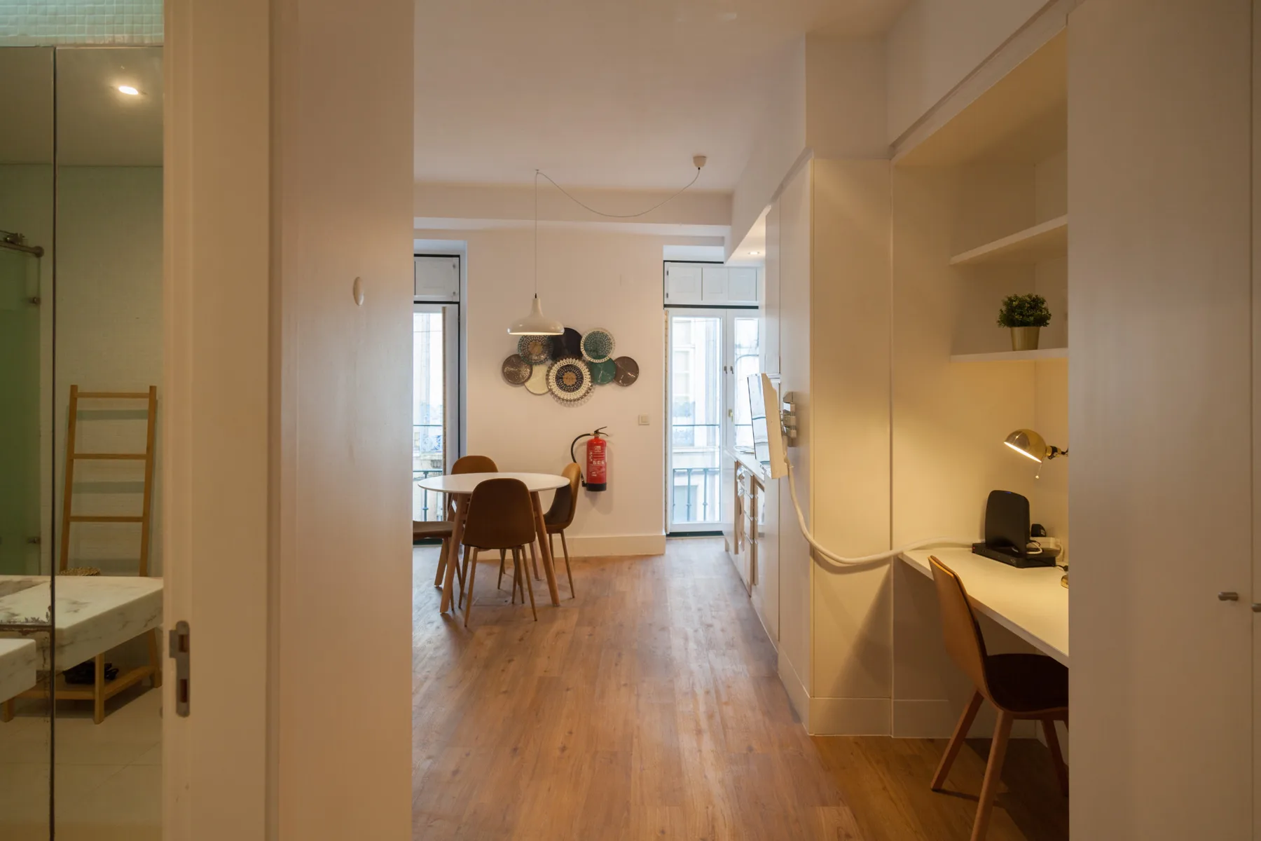 Un estudio luminoso tiene una mesa de comedor y un escritorio junto a la pared derecha.