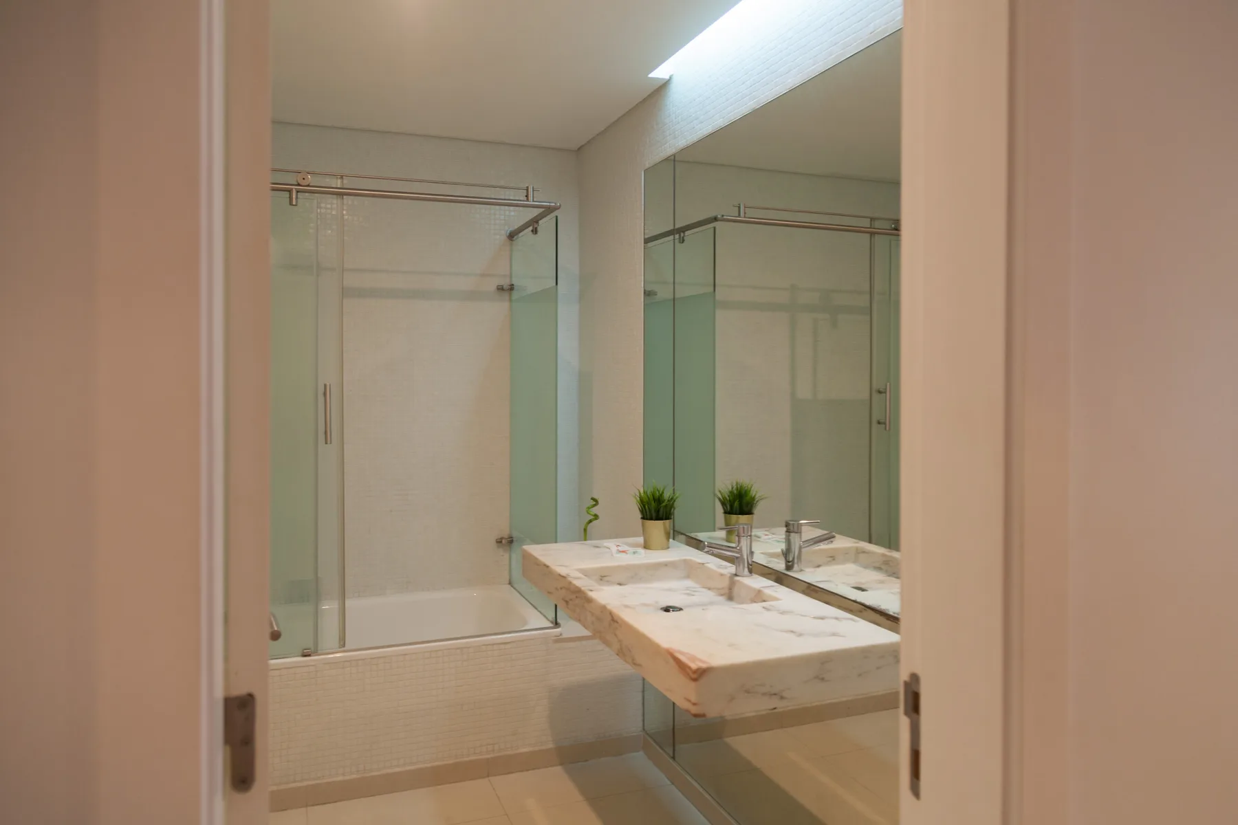 Un baño con ducha de vidrio y un lavabo de mármol bajo un espejo grande.