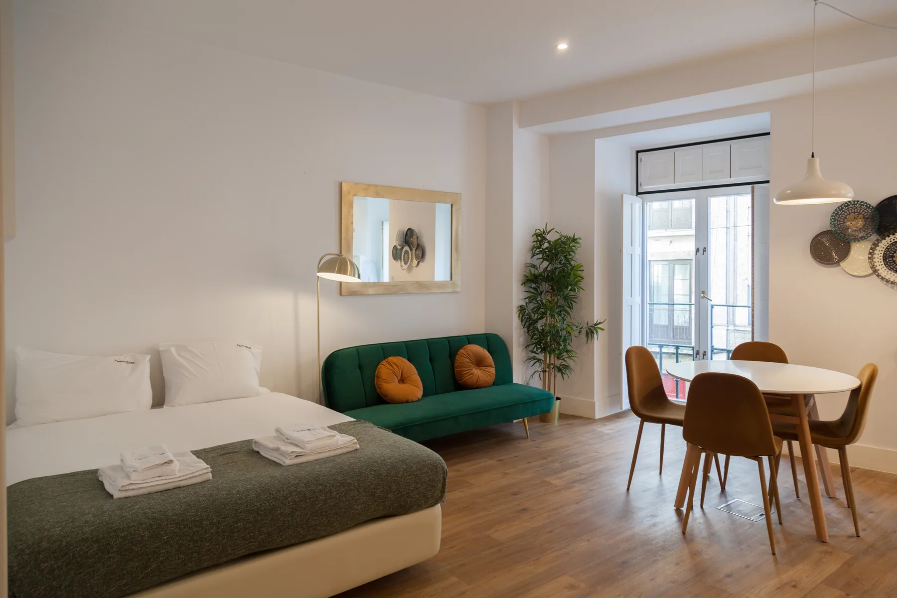 Un estudio con una cama, asientos verdes y una mesa de comedor junto a la ventana.