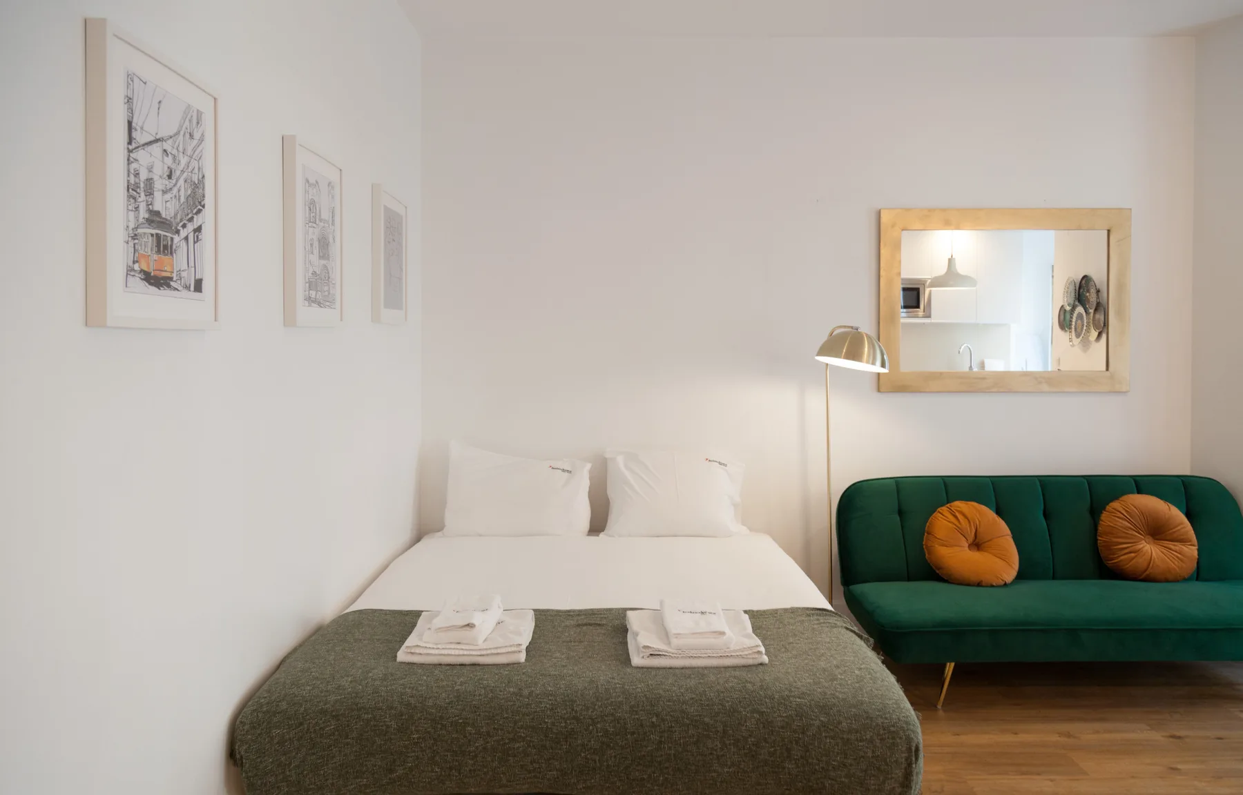 Un dormitorio con una cama, un sofá verde y cuadros en la pared.