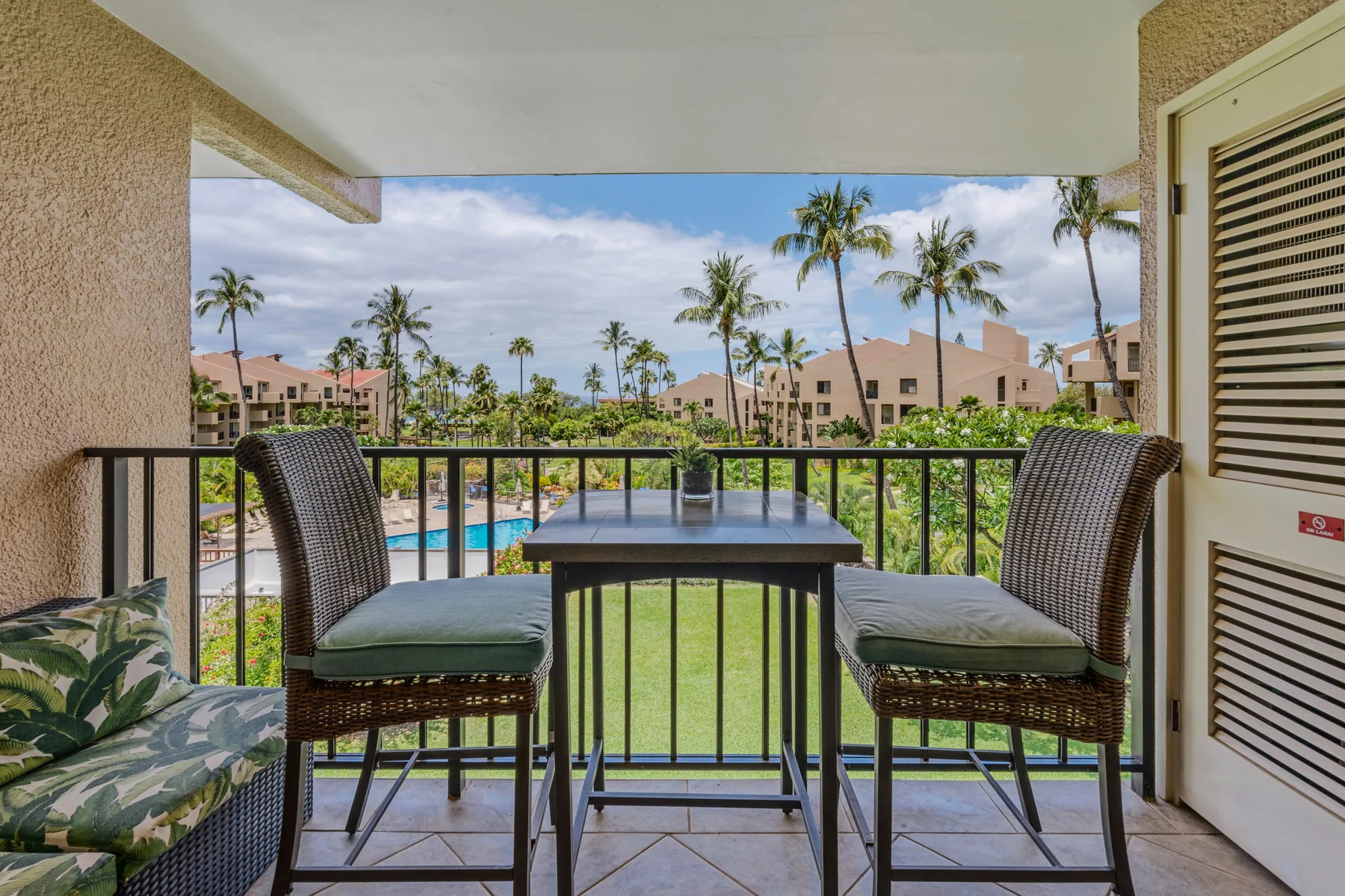 A balcony seating area overlooks a pool and palm trees.