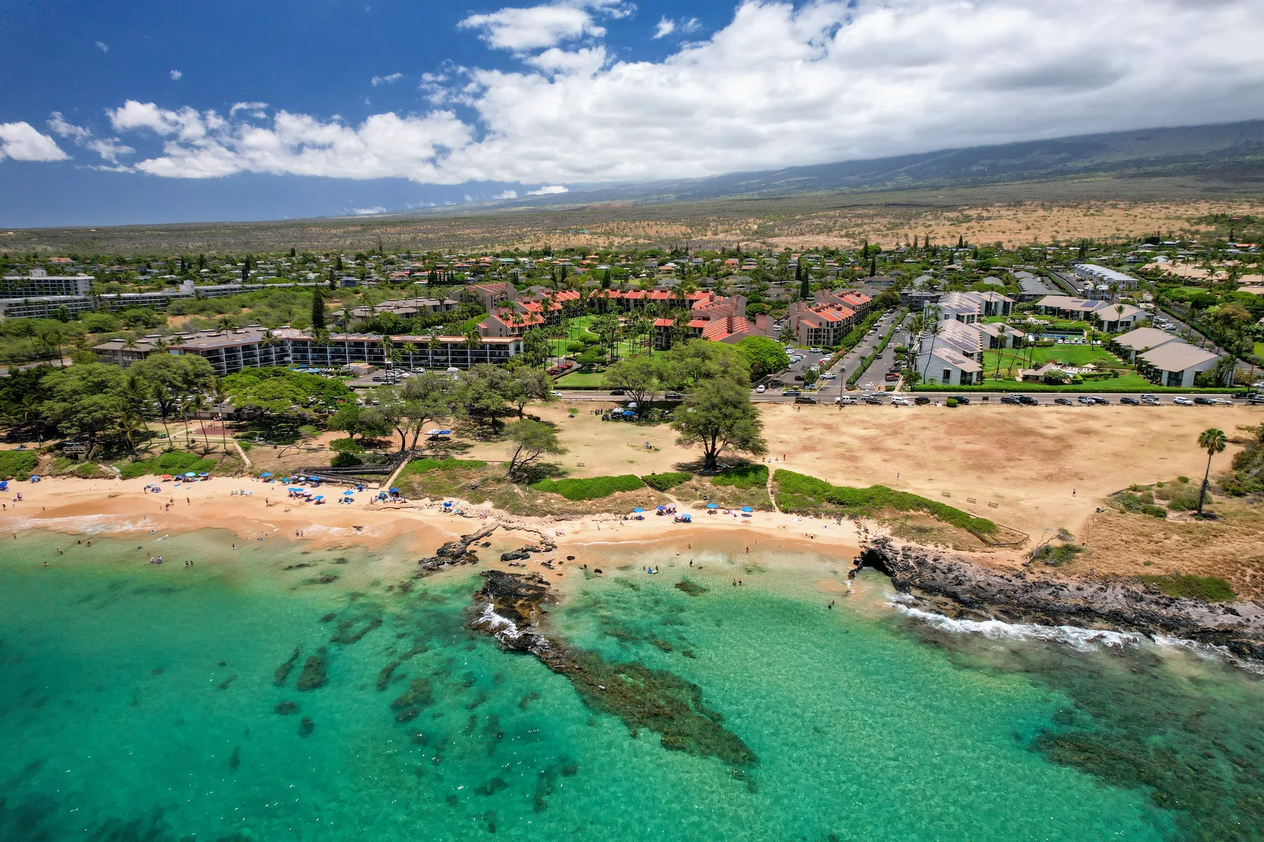 An aerial view of a sandy beach and turquoise water beside a coastal town.