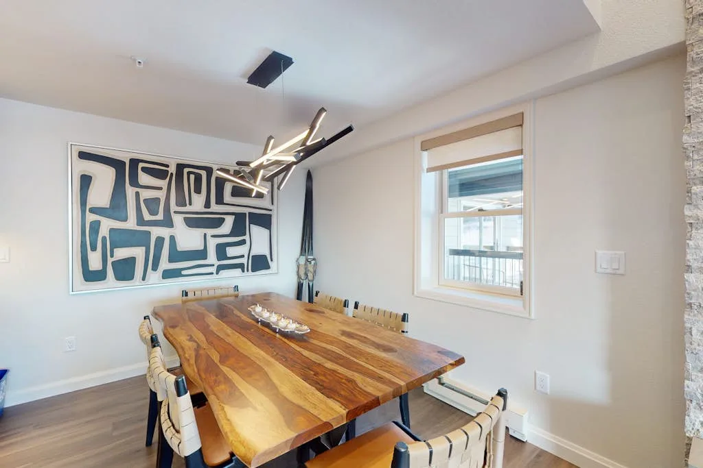 Comedor con una larga mesa de madera bajo una lámpara moderna.