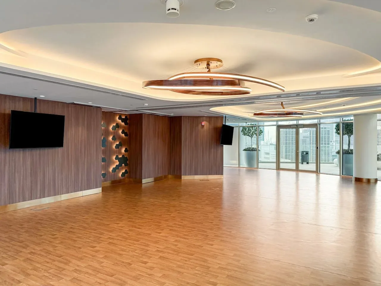 A spacious event room with a wood floor, wall screens, and glass doors.
