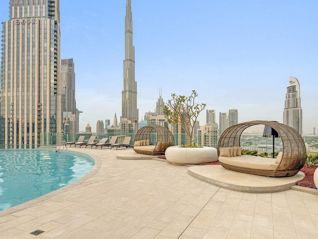 A rooftop pool deck with curved lounge seating and a city skyline beyond.